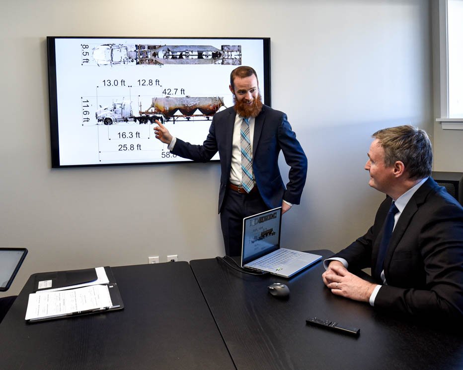 Forensic engineer in a suit presenting technical findings to an attorney during a conference room meeting.