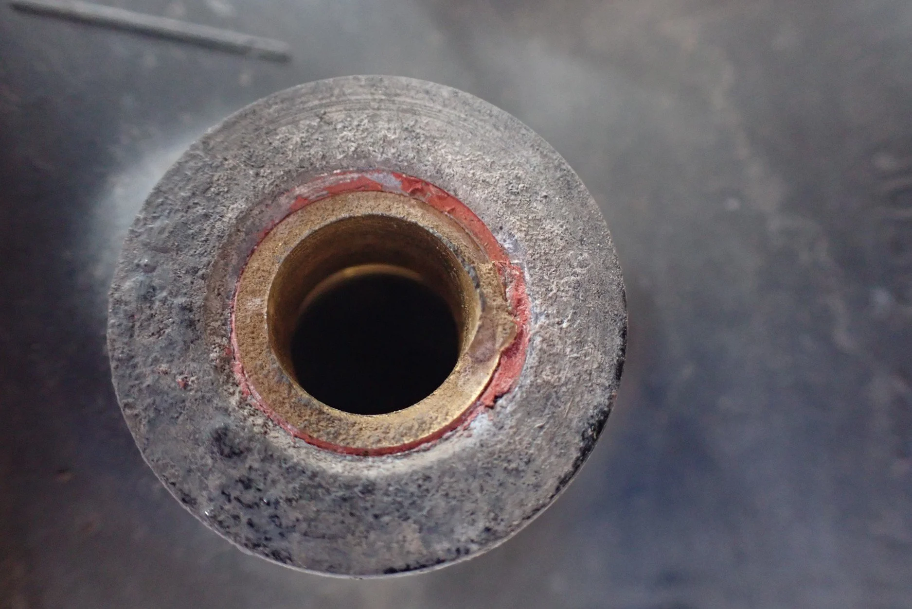 Close-up of a rusted metal pipe or tube opening, viewed from above, with surrounding rough metal surface.