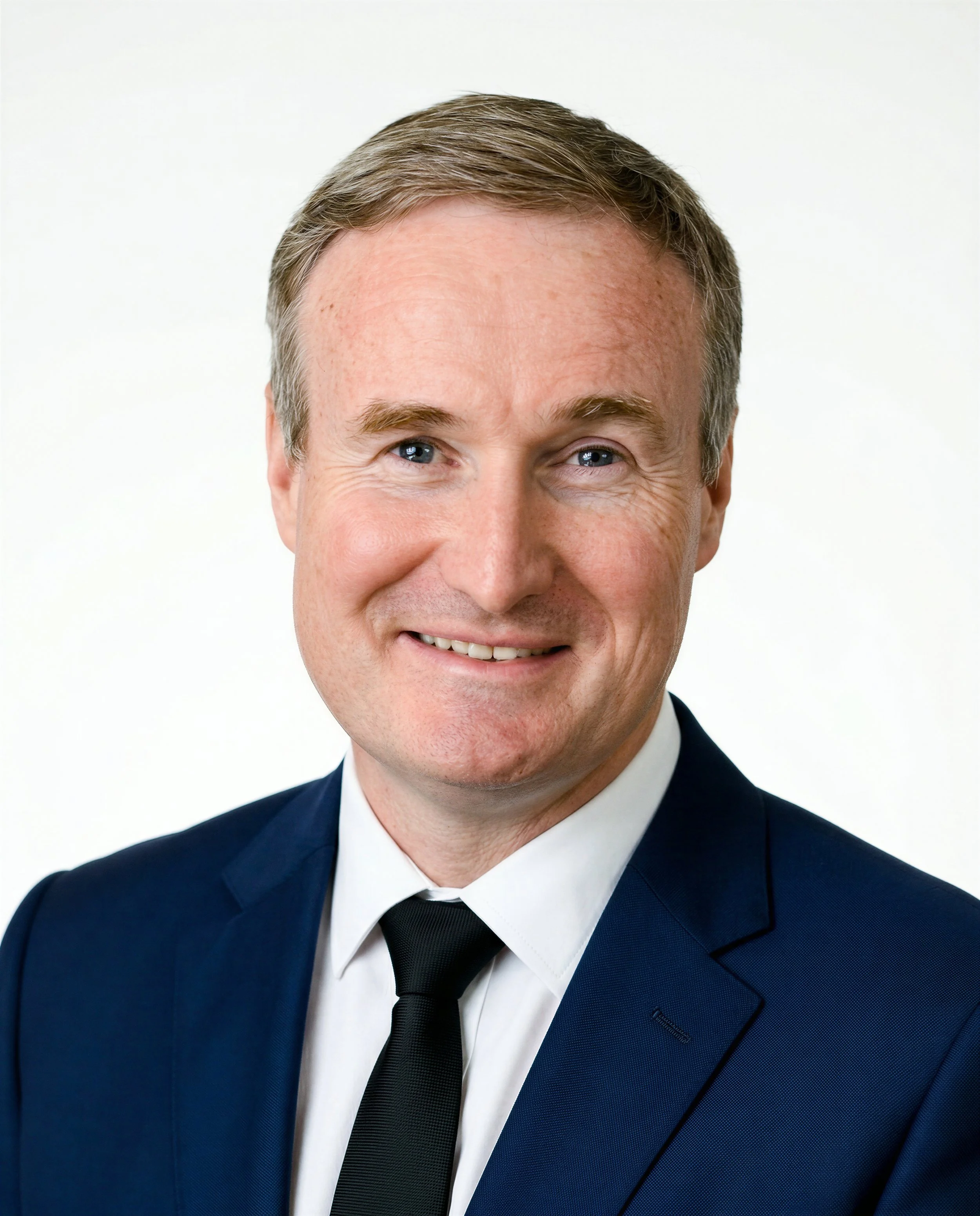 Professional man in a business suit smiling, sitting against a plain background.