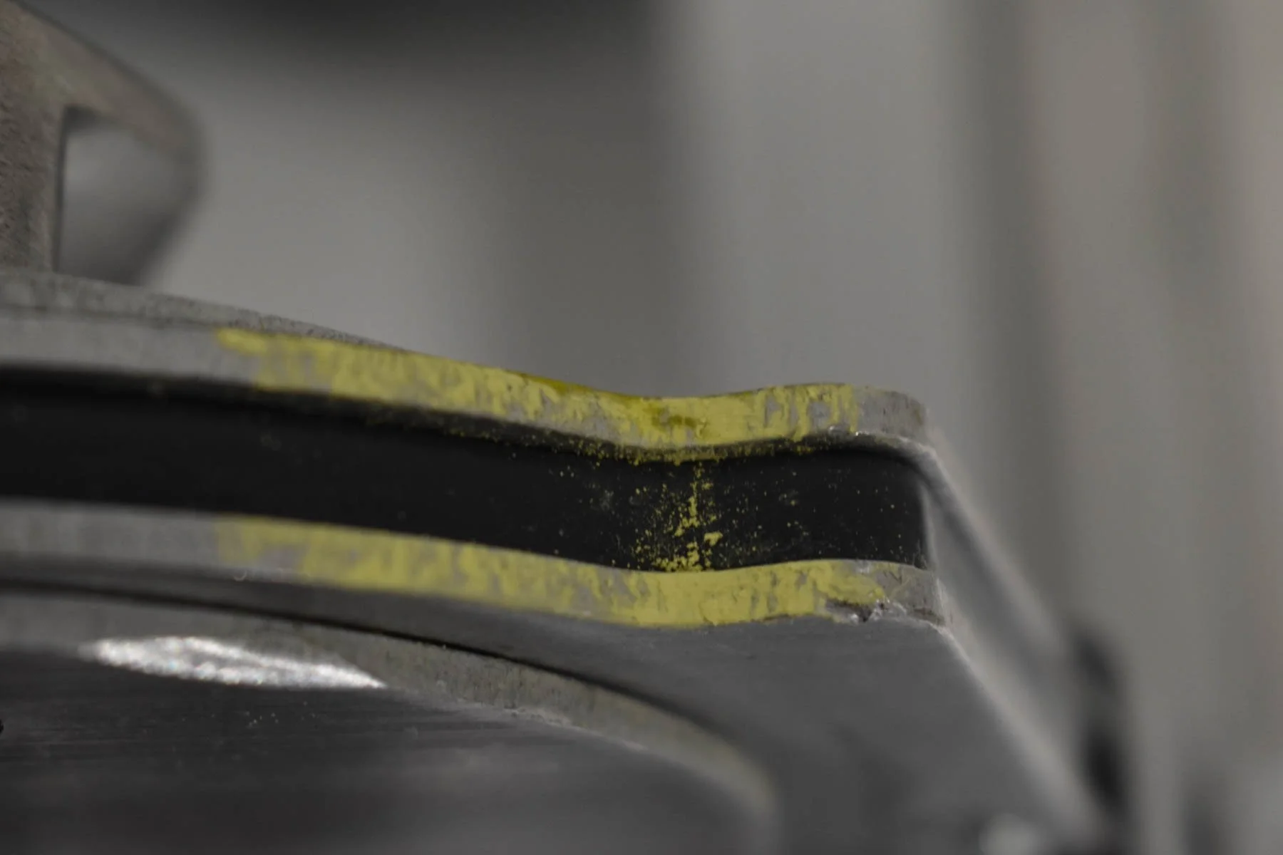 Close-up of a rugged metallic tool or object with yellow paint chips, showing signs of wear and aging.
