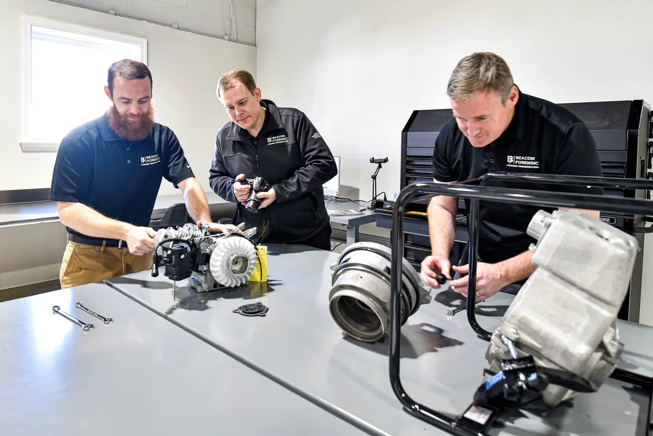 Three forensic engineers inspecting a pump motor in a laboratory, one holding a tool and the other using a camera.