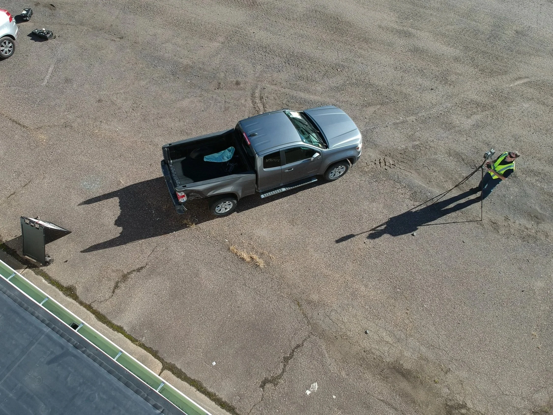 Aerial view of an engineer conducting accident reconstruction while inspecting a crash-damaged vehicle in a storage yard, documenting damage and evidence.