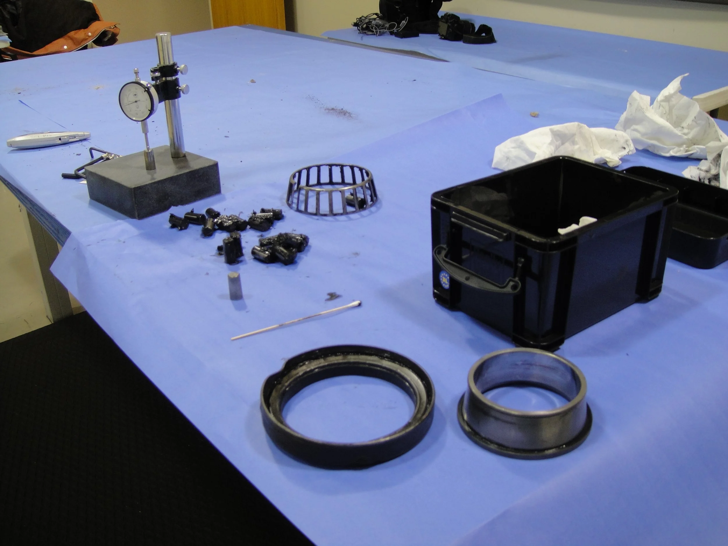 Laboratory table with a blue cover where a disassembled tapered roller bearing is being inspected, with measurement tools visible on the surface