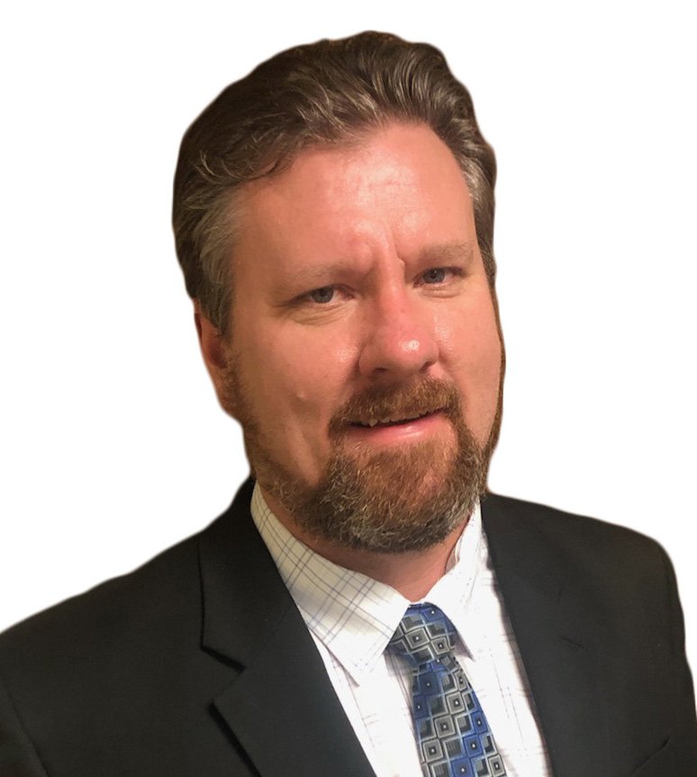 A middle-aged man with light skin, a full beard, and styled gray hair, wearing a dark suit, white shirt, and a patterned tie, posing against a white background.