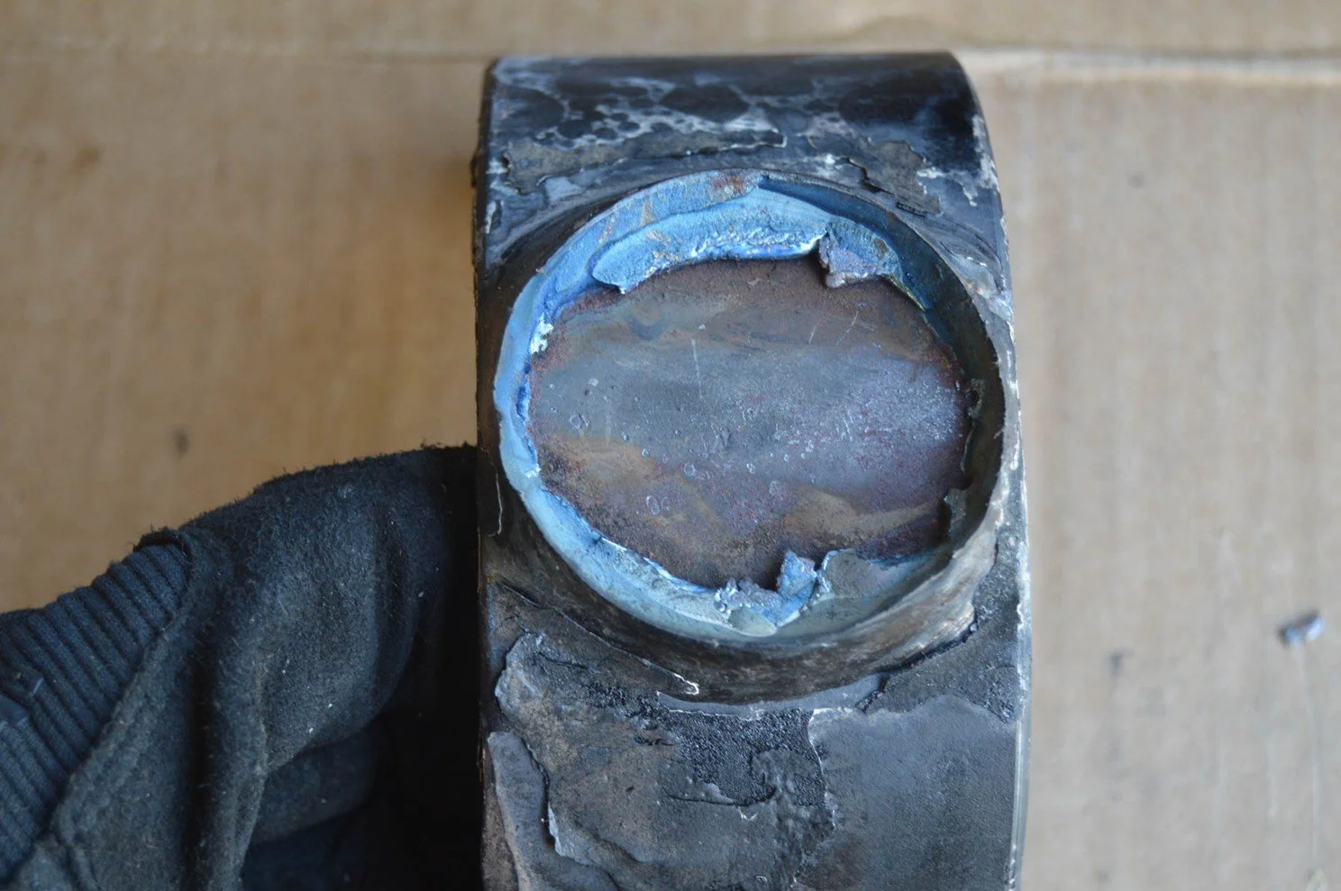 Close-up of a worn, scratched metal shaft with a rusted, damaged circular end, held by a gloved hand.