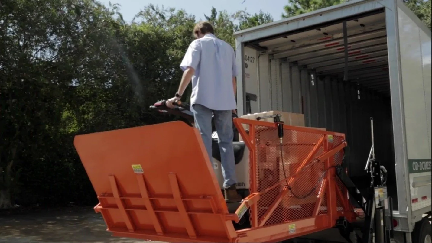 Detailed technical diagram of a mechanical lifting device with labeled components including main control handle, remote control cable, upper lifting arm, control valve, lifting lug, ECS valve switch, bridge, automatic folding ramp, platform, main lifting arm, platform locking pin, hydraulic cylinder, frame, stabilizing jack, castor wheel, and fixed wheel.