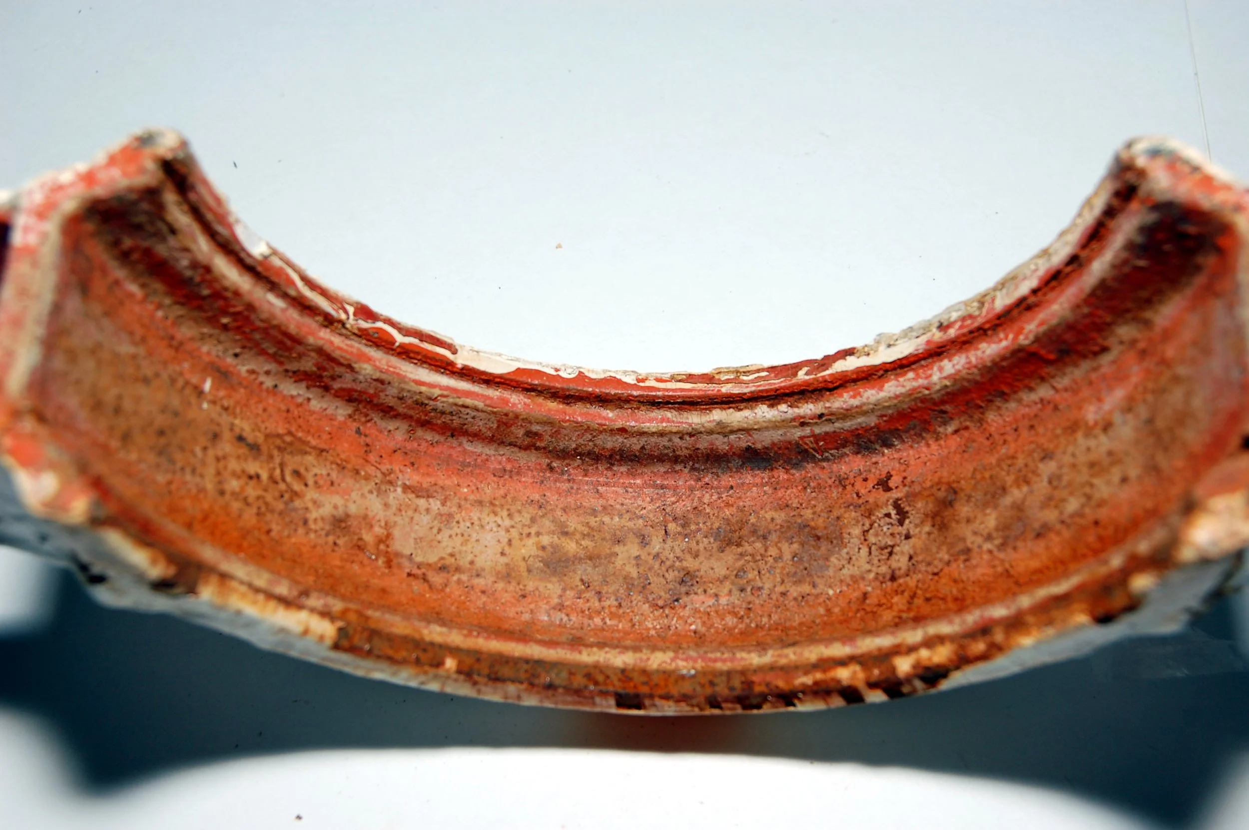 Close-up of a weathered, rust-colored metal object with a curved shape and chipped edges.