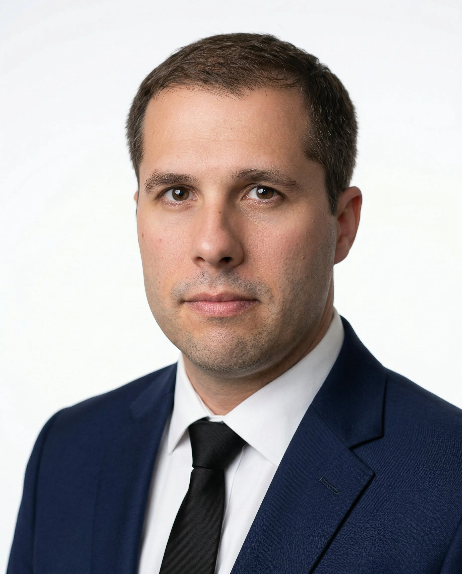 Headshot of a man with short dark hair, wearing a suit and blue shirt, against a gray background.