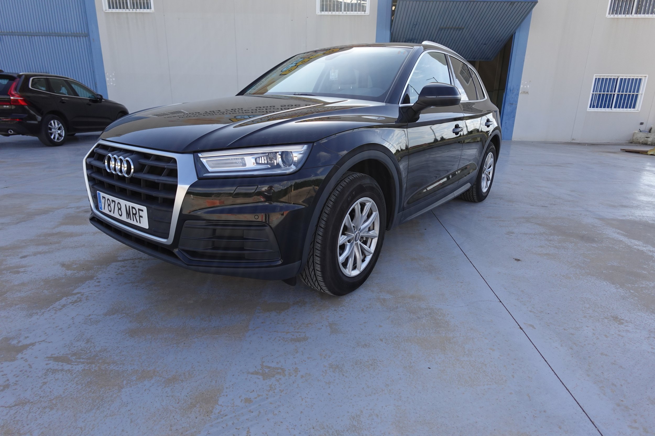A black Audi SUV parked on a concrete surface outside a building with blue and white exterior walls.