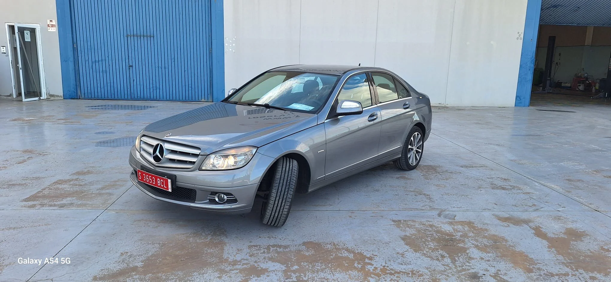Interior of a silver van showing two rows of seats, with the driver's seat and dashboard on the right side and a three-seater bench on the left side.