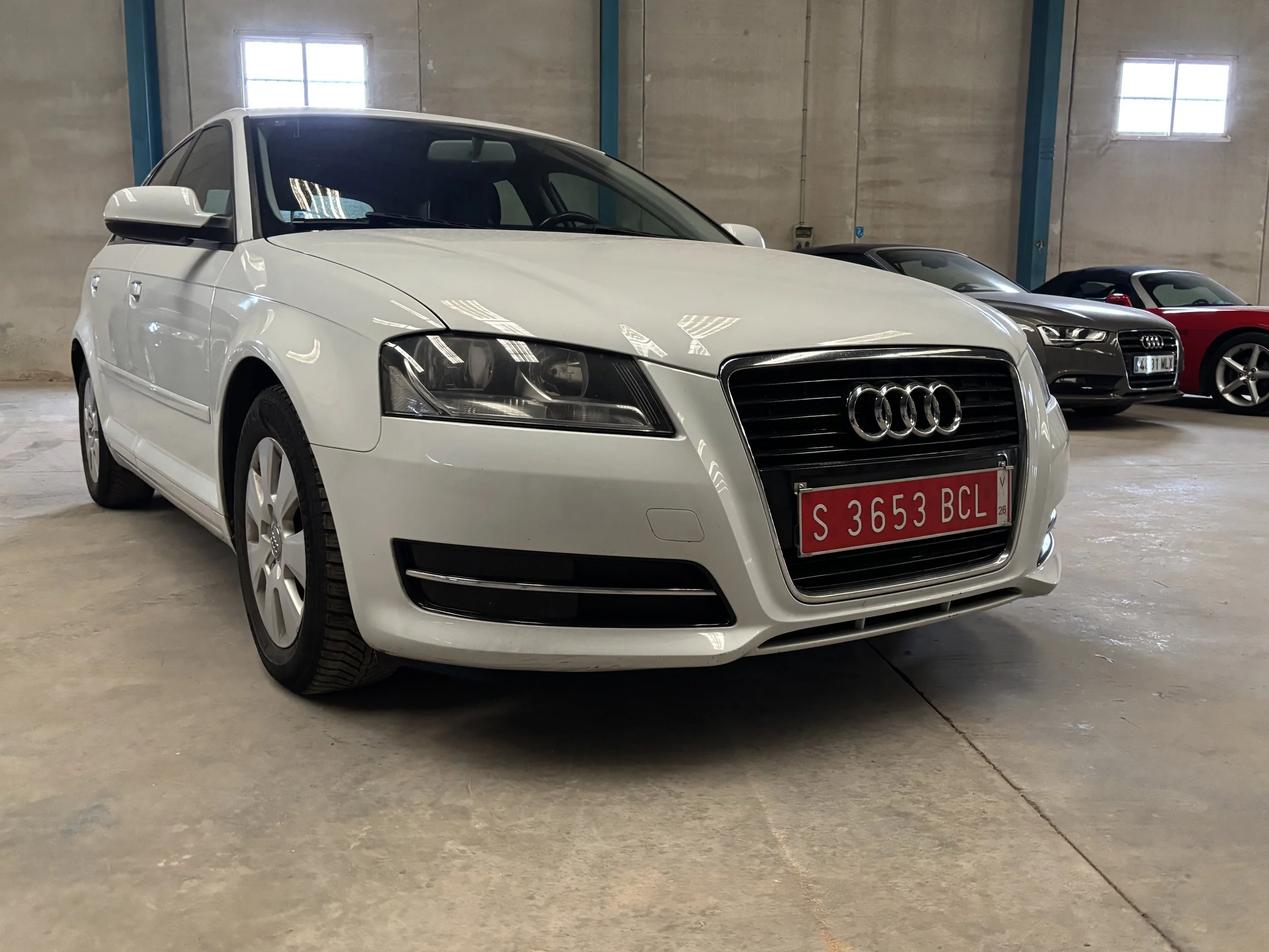 Inside a vehicle, view of the black steering wheel with a Renault logo, dashboard with speedometer, tachometer, fuel gauge, and a small digital display showing temperature and other indicators. To the right, part of the climate control system and center console are visible.