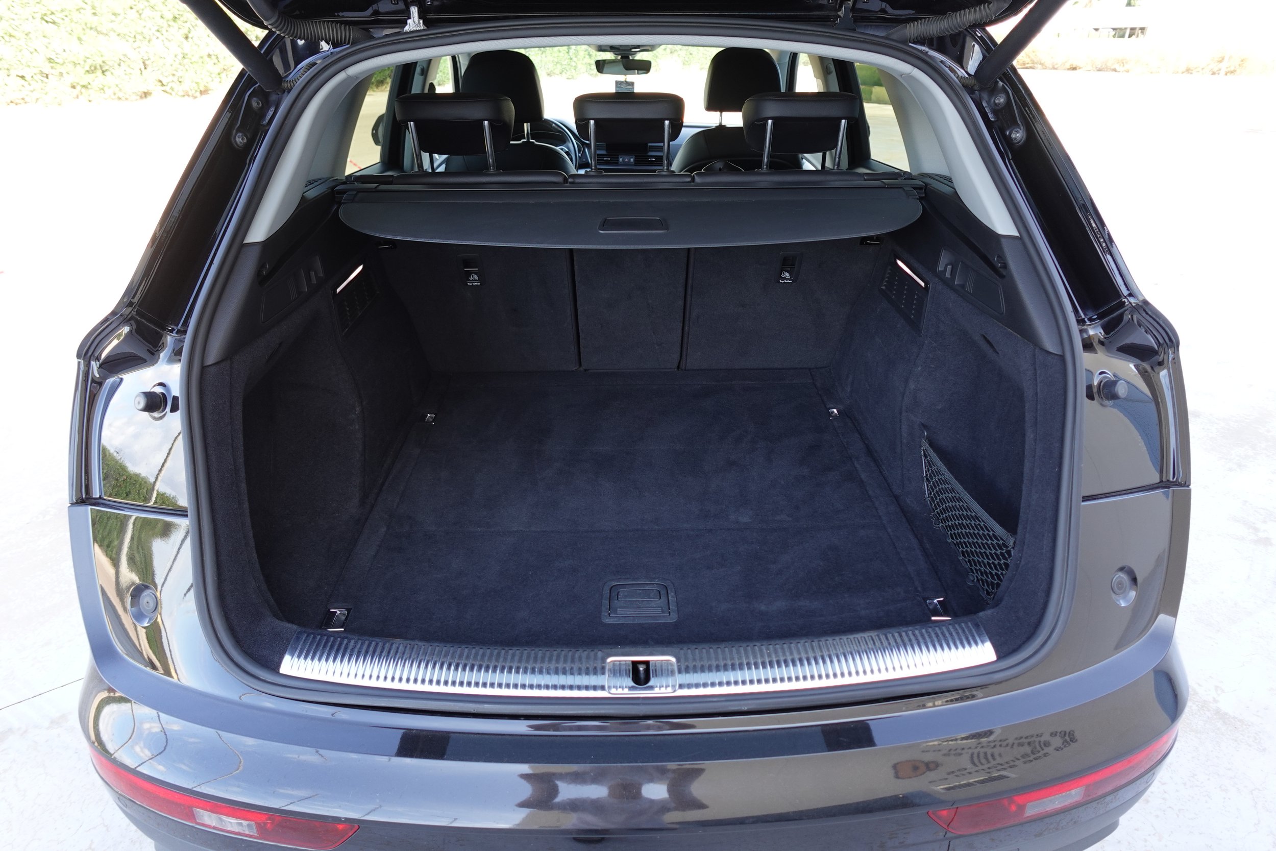 Open trunk of a black SUV, showing a spacious cargo area with black carpeting, a retractable cargo cover, and rear seats.