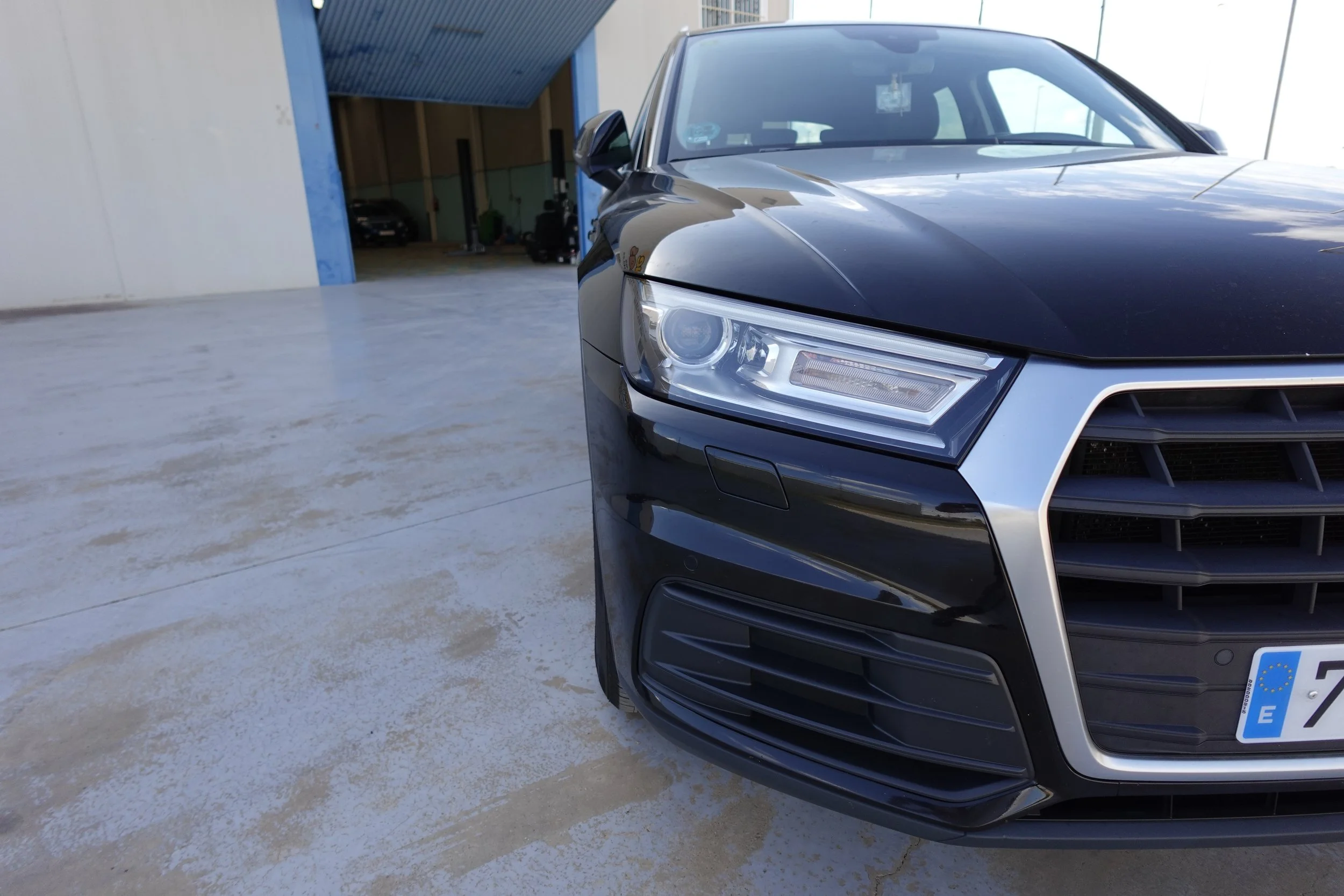 Close-up of the front right side of a black luxury car parked outside a building with a large open garage door