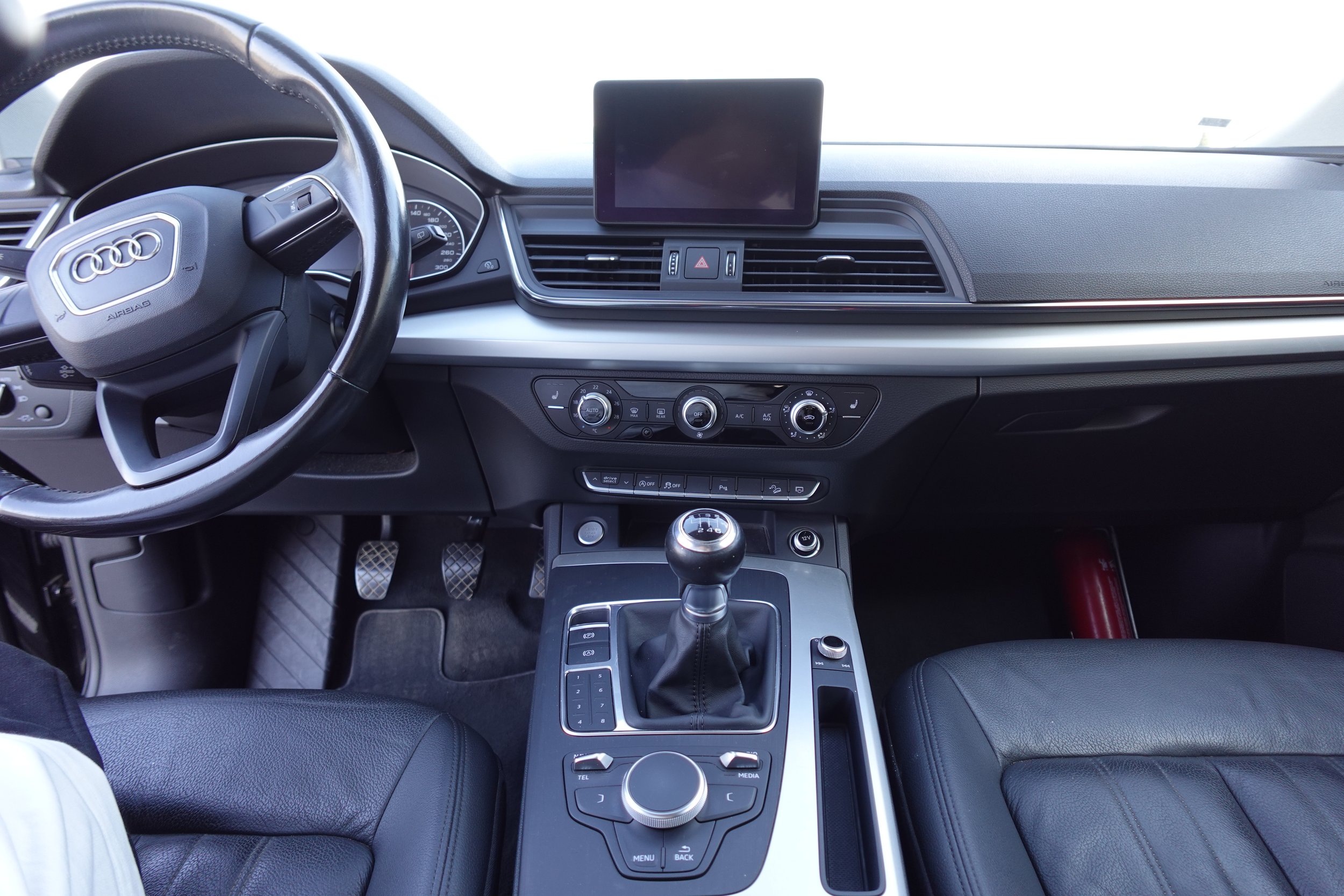 Interior of a modern car dashboard with steering wheel, gear shift, infotainment screen, and climate controls.