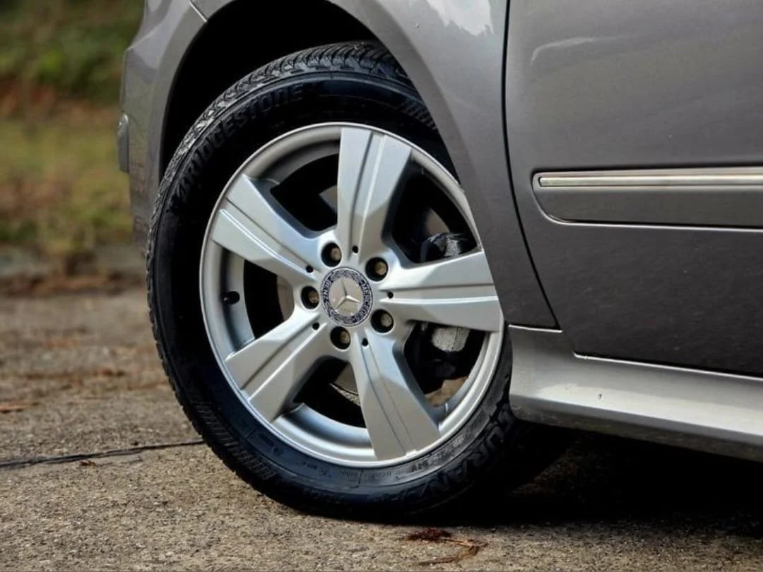 Interior of a silver van showing two rows of seats, with the driver's seat and dashboard on the right side and a three-seater bench on the left side.