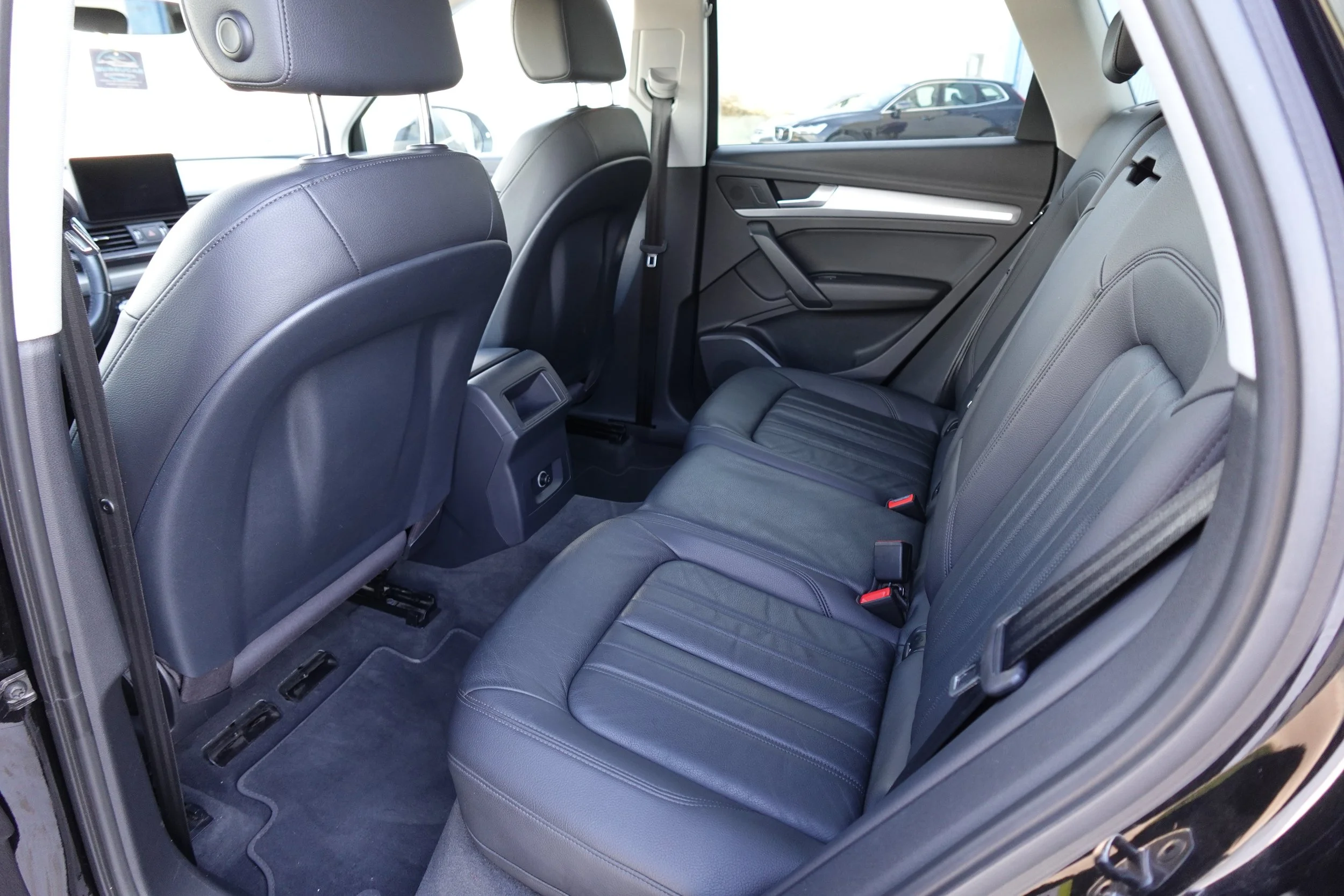 The interior of a black SUV showing the second row of black leather seats, rear of the front seats, and part of the vehicle's window with parked cars outside.