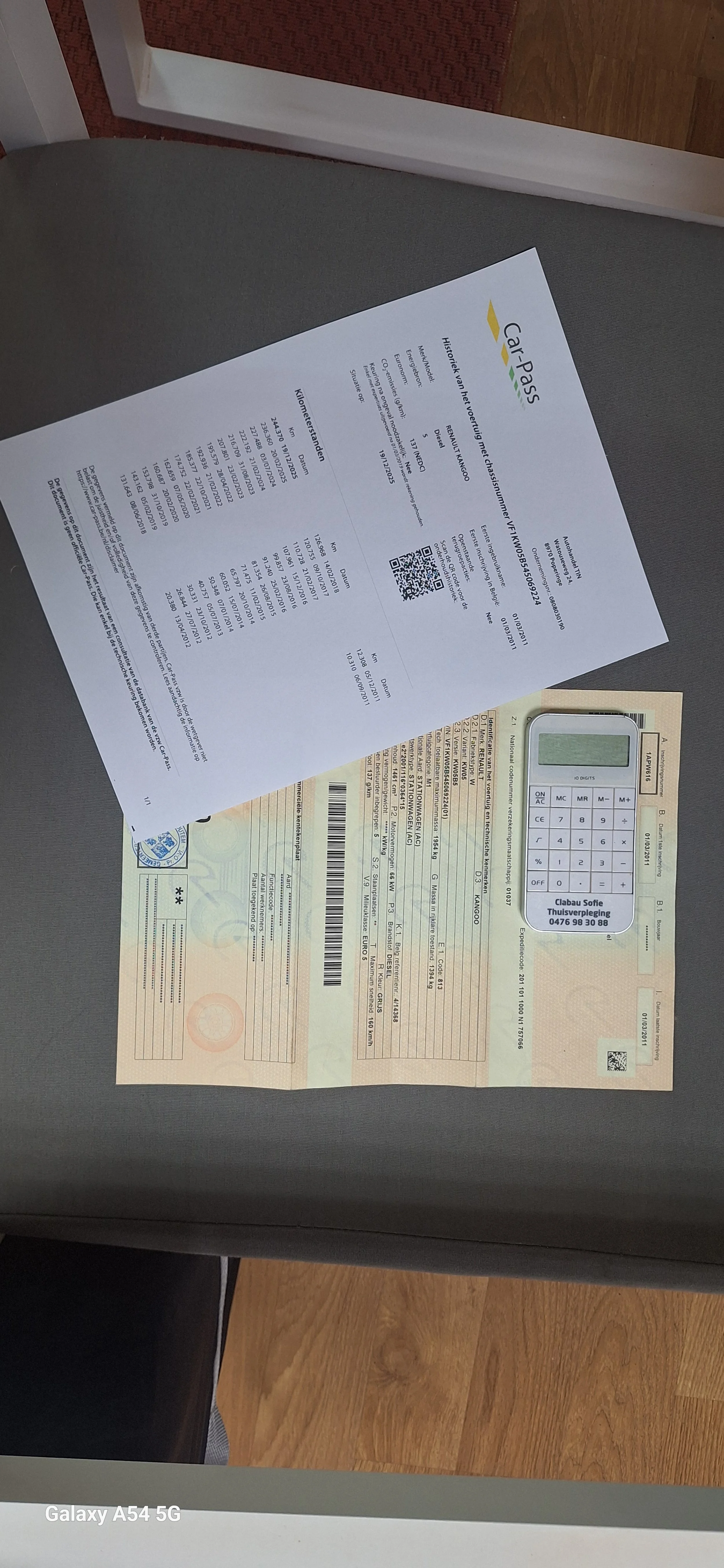 A car inspection report and a vehicle registration document on a gray surface, with a small calculator placed on top of the registration paper.