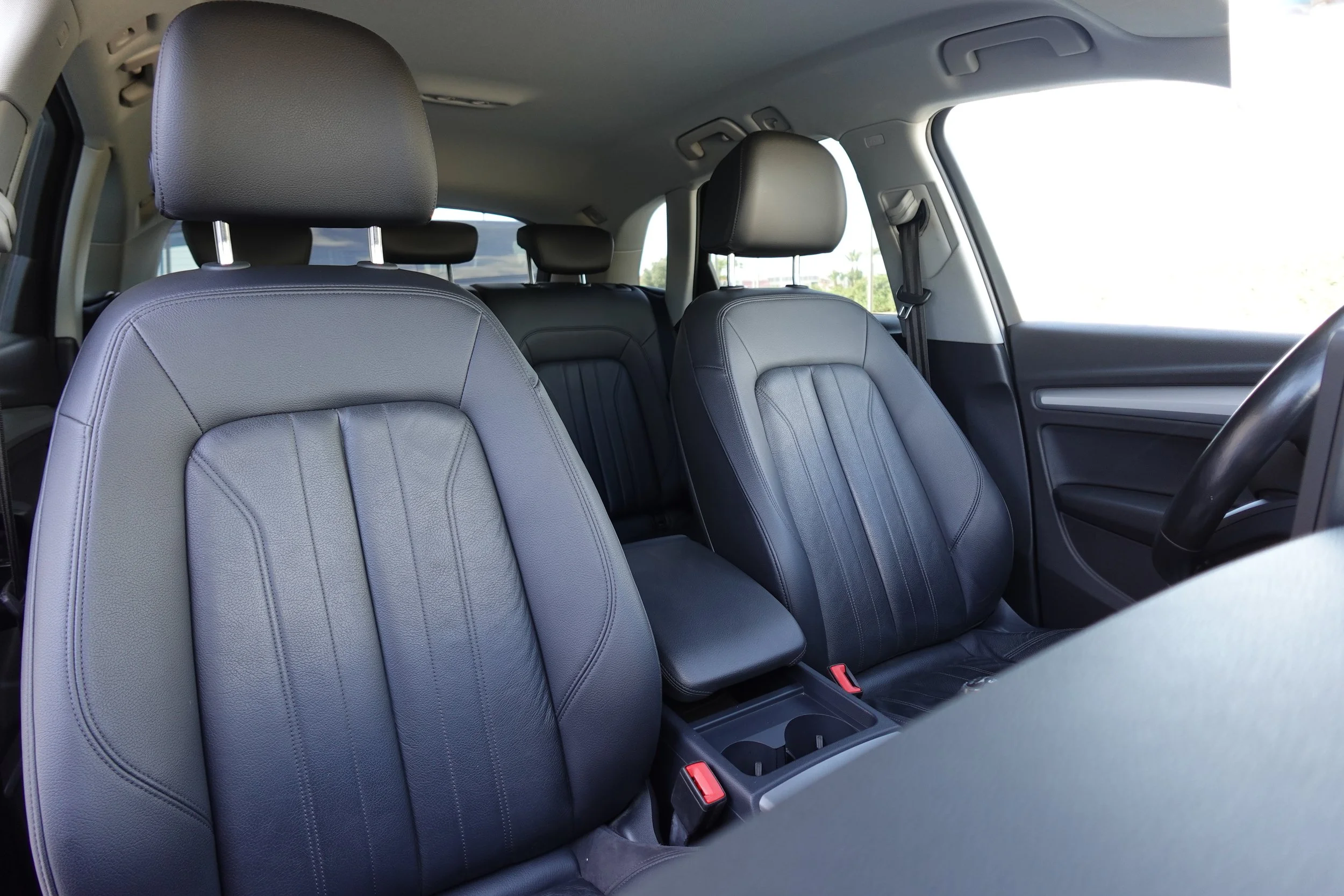 The interior of a car showing the front two black leather seats with headrests, a middle seat with a fold-down armrest, and the front passenger side door with a window.