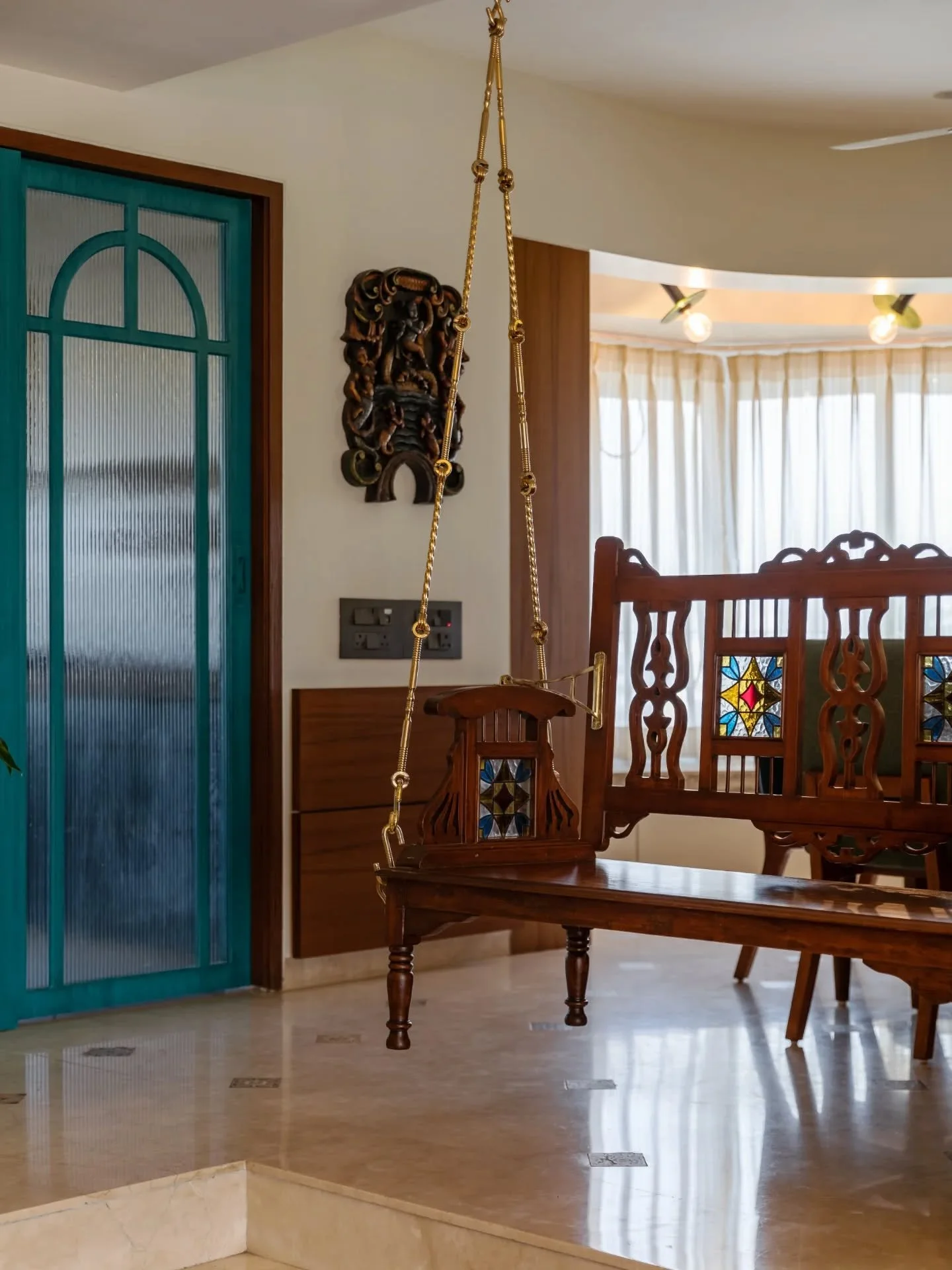 This is where nostalgia meets good light. The living room features patterned Indian flooring, a rocking chair in one corner, planters in another, and art that feels handpicked from memory. The dining glows under patterned wallpaper with a secret bar,