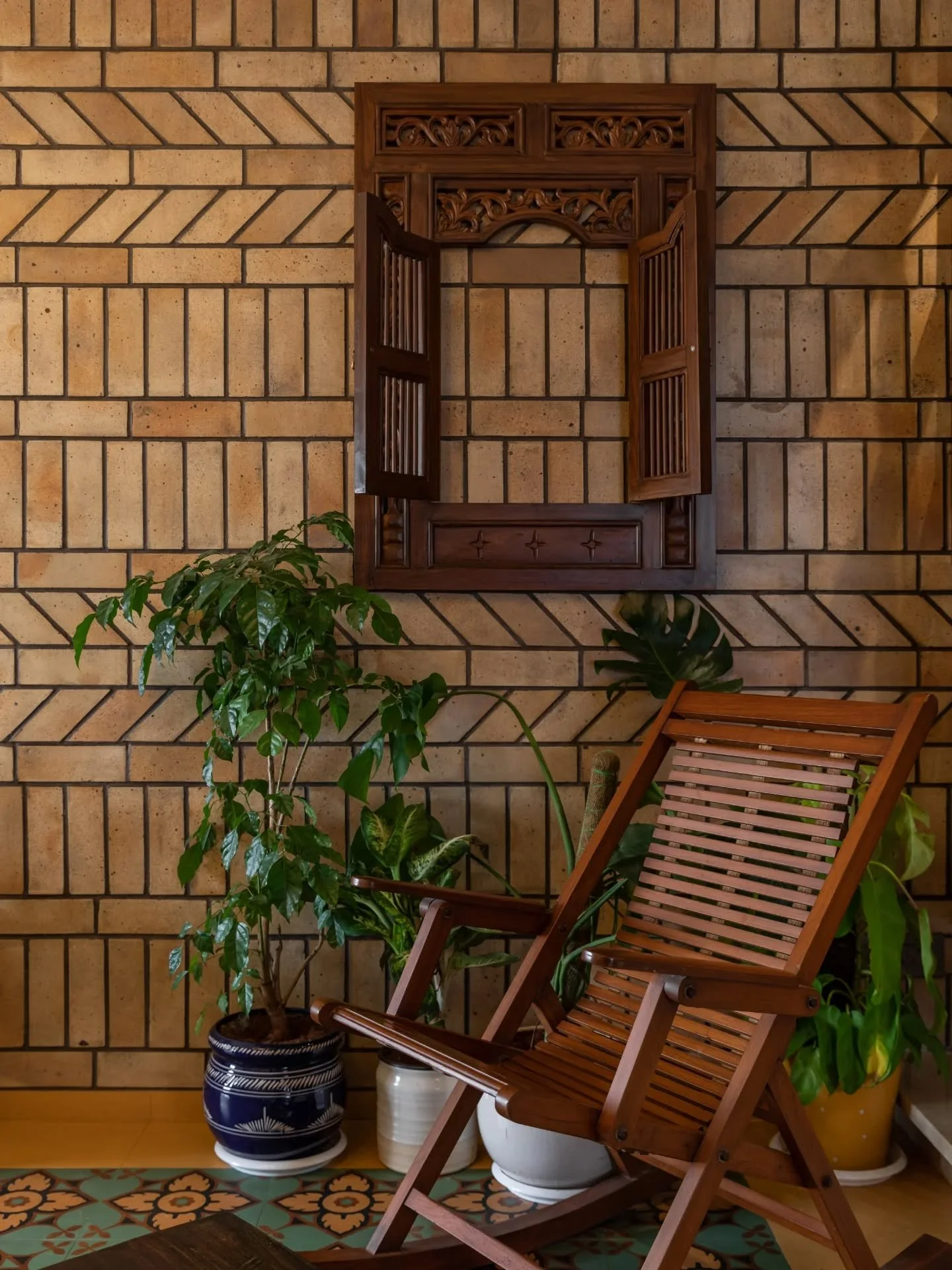 A wooden mirror catches the foyer&rsquo;s golden light, while a Ganpati sculpture quietly anchors the space. The living wall holds a framed window from another time; planters soften brick and metal. Even the tucked-in bar feels intentional &mdash; de