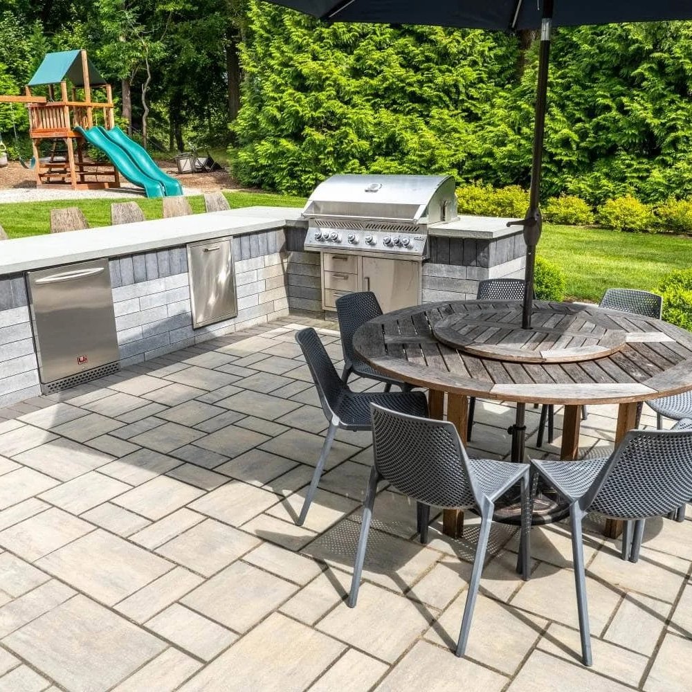 A high-end backyard retreat featuring a custom outdoor kitchen design with stone cabinetry and grill station in Woodcliff Lake, NJ
