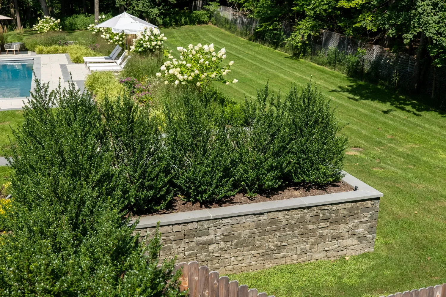 Retaining wall supporting a raised planting area along a wooded property line in Upper Saddle River, NJ