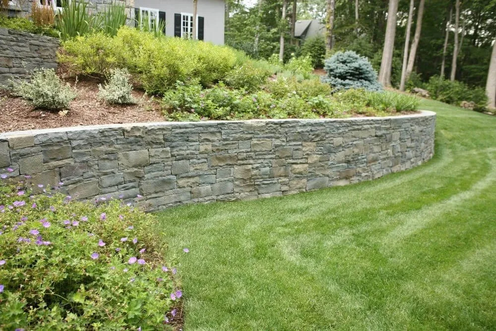 Functional backyard retaining wall with natural stone finish supporting a raised lawn and garden
