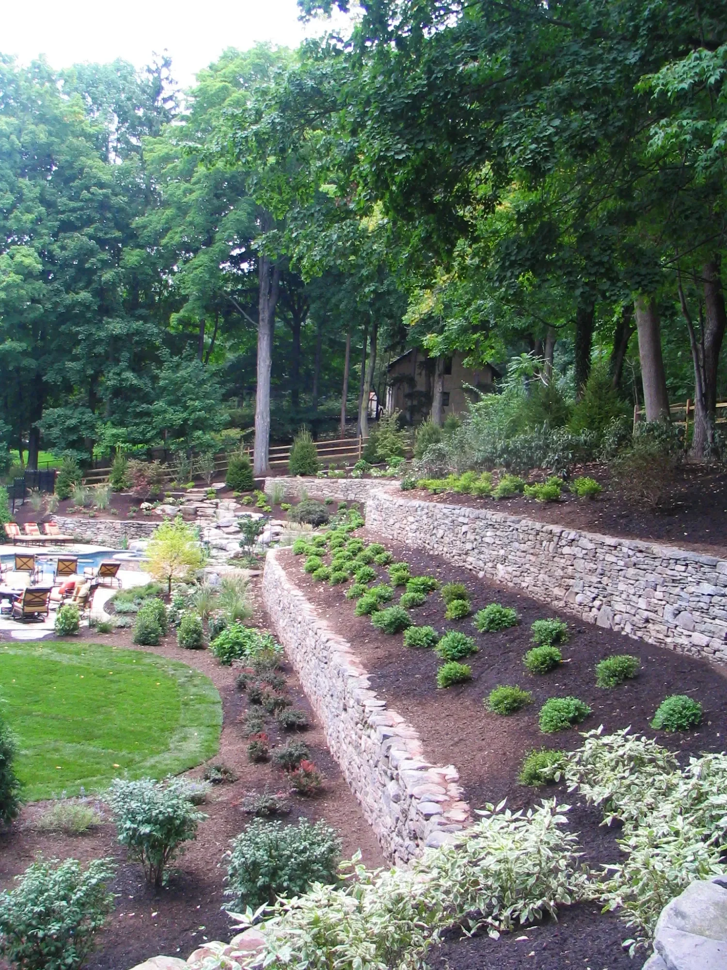 Long retaining wall stabilizing a sloped backyard with layered shrubs in Upper Saddle River, NJ