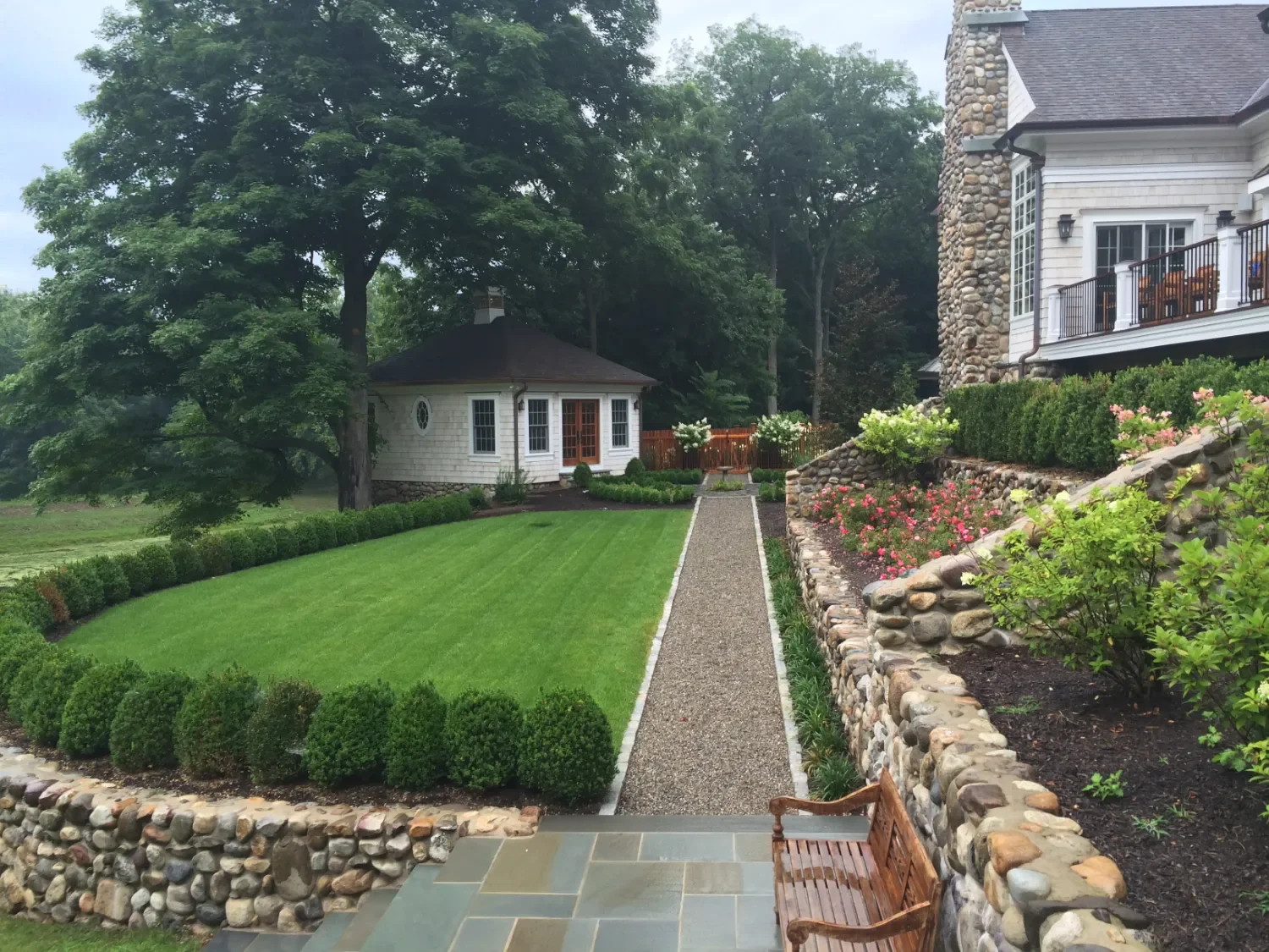 Stone retaining wall guiding a narrow garden walkway with manicured plantings in Upper Saddle River, NJ