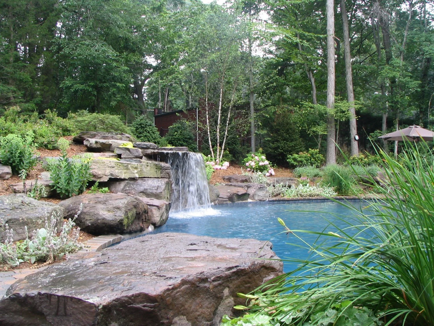 Backyard pool with integrated rock waterfall and natural stone coping in Ho-Ho-Kus, NJ