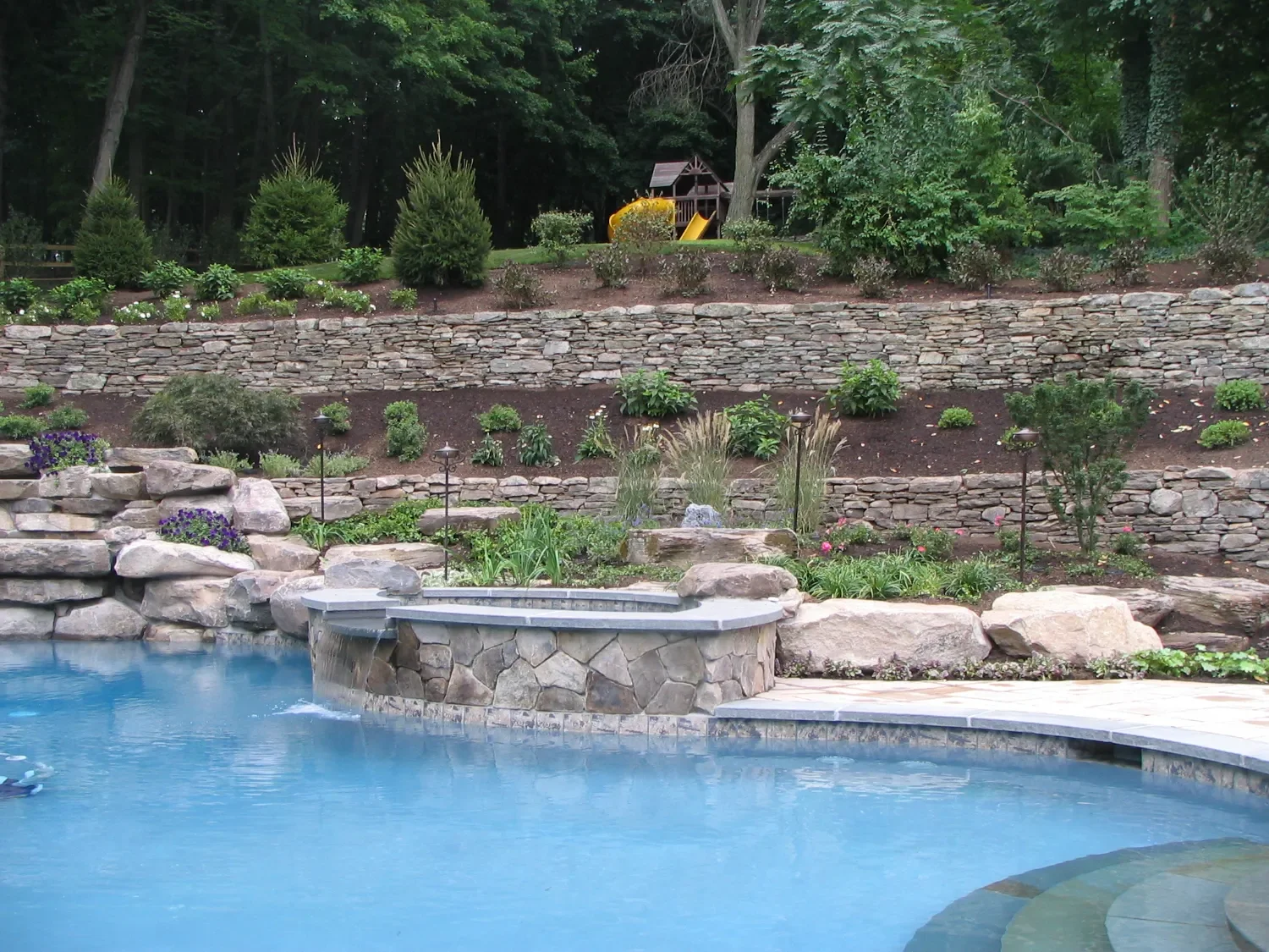 Tiered retaining wall integrated with a pool landscape and planting beds in Ridgewood, NJ