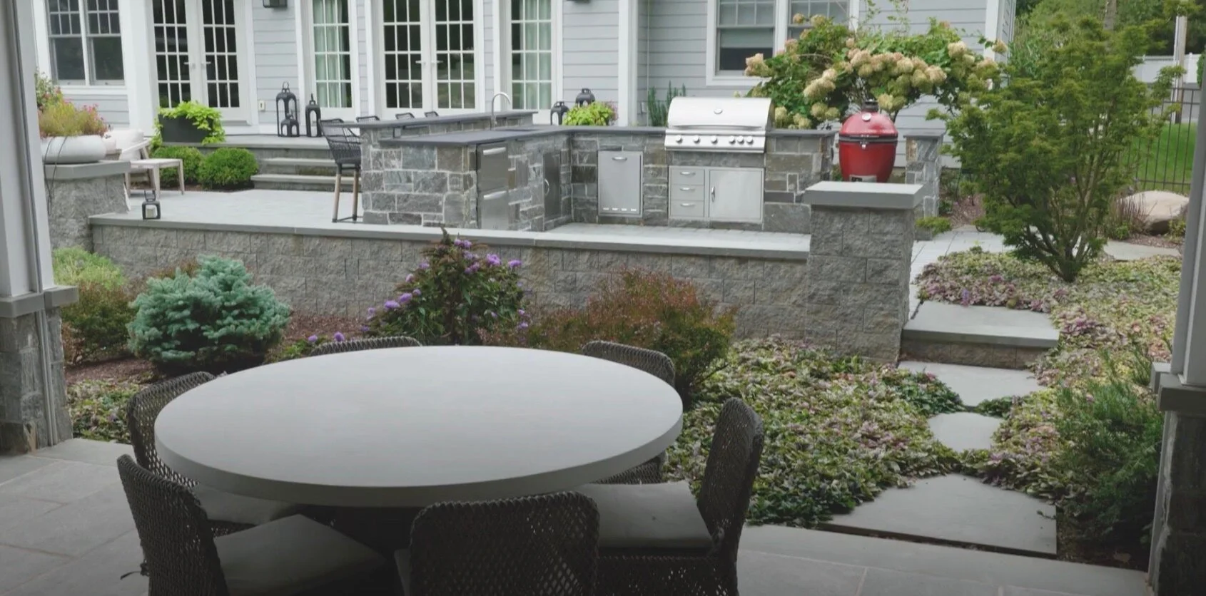 Outdoor kitchen with built-in grill, natural stonework, and garden seating area in Glen Rock, NJ.jpg