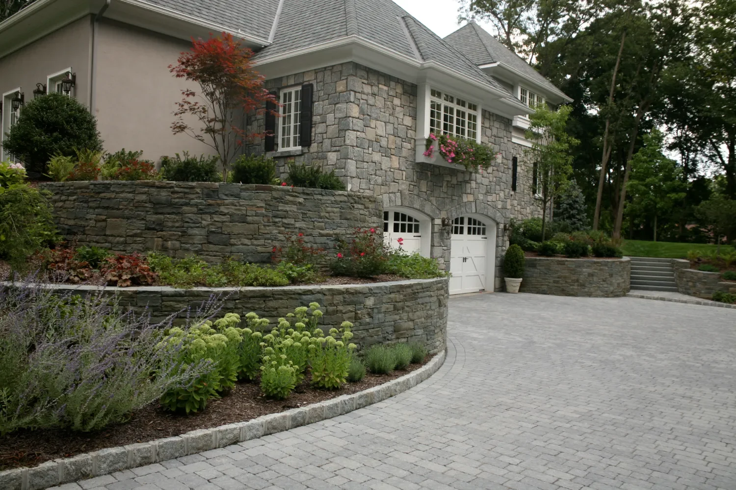 Curved retaining wall built with natural stone supporting a driveway edge in Oradell, NJ