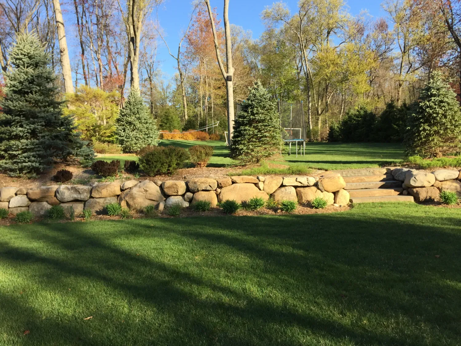 Boulder-style retaining wall framing a lawn and mature trees in Oradell, NJ
