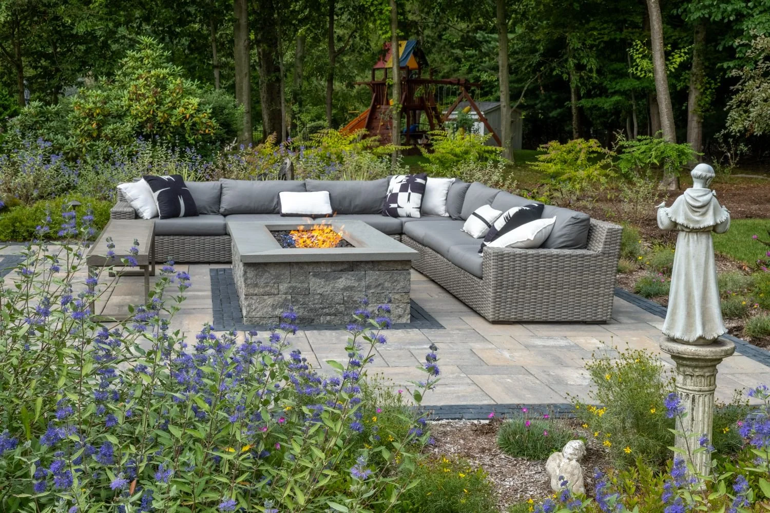 A fire pit paired with sectional seating beneath mature trees in Ridgewood, NJ