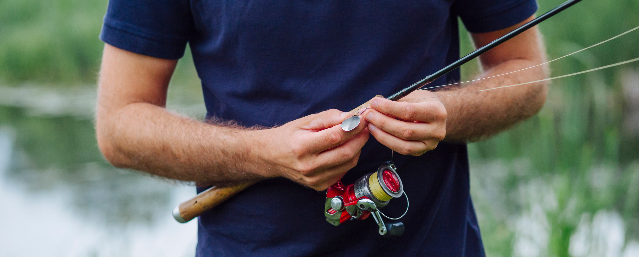A person holding a fishing rod and preparing fishing tackle near water.