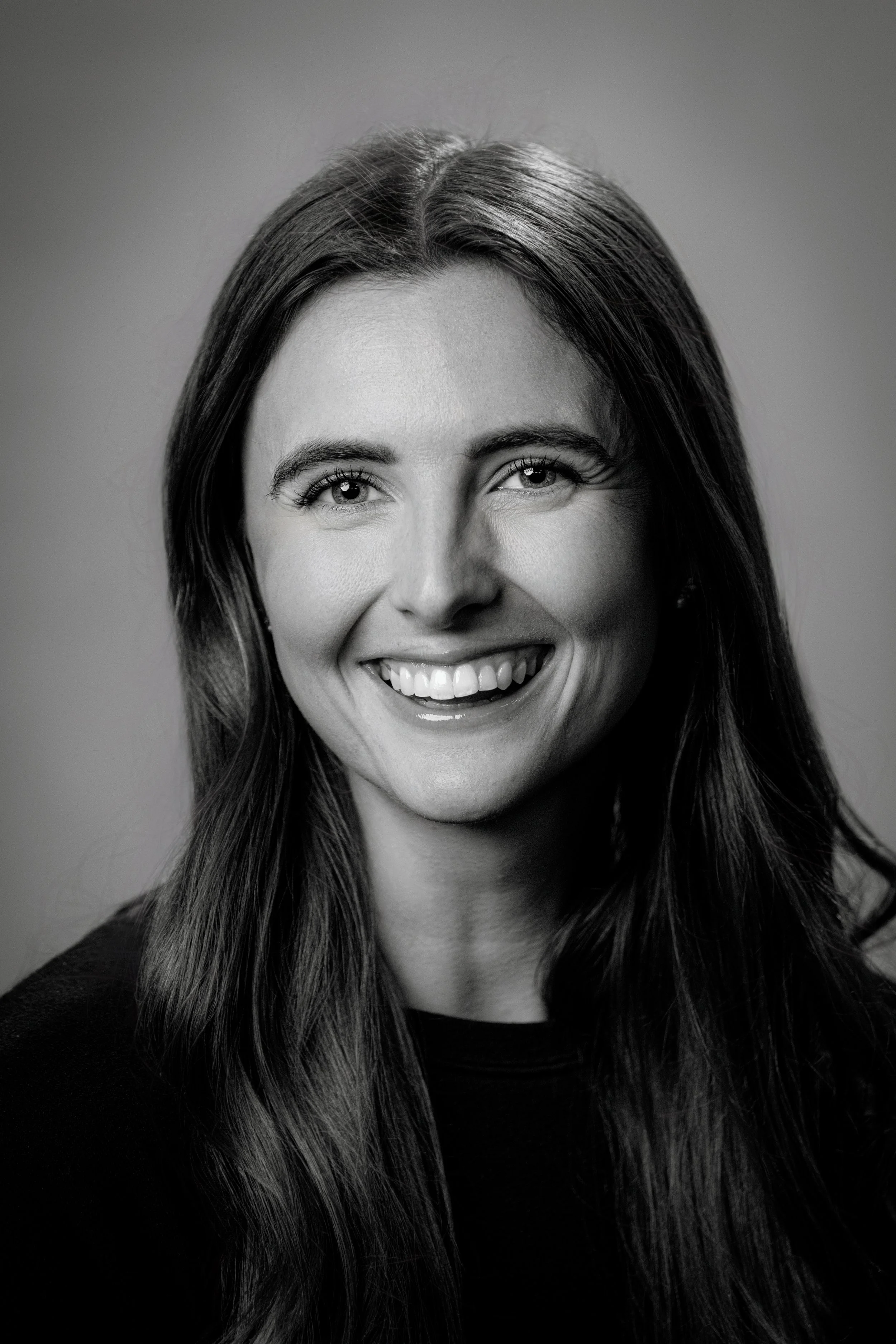 Black and white portrait of a smiling woman with long hair, looking directly at the camera.