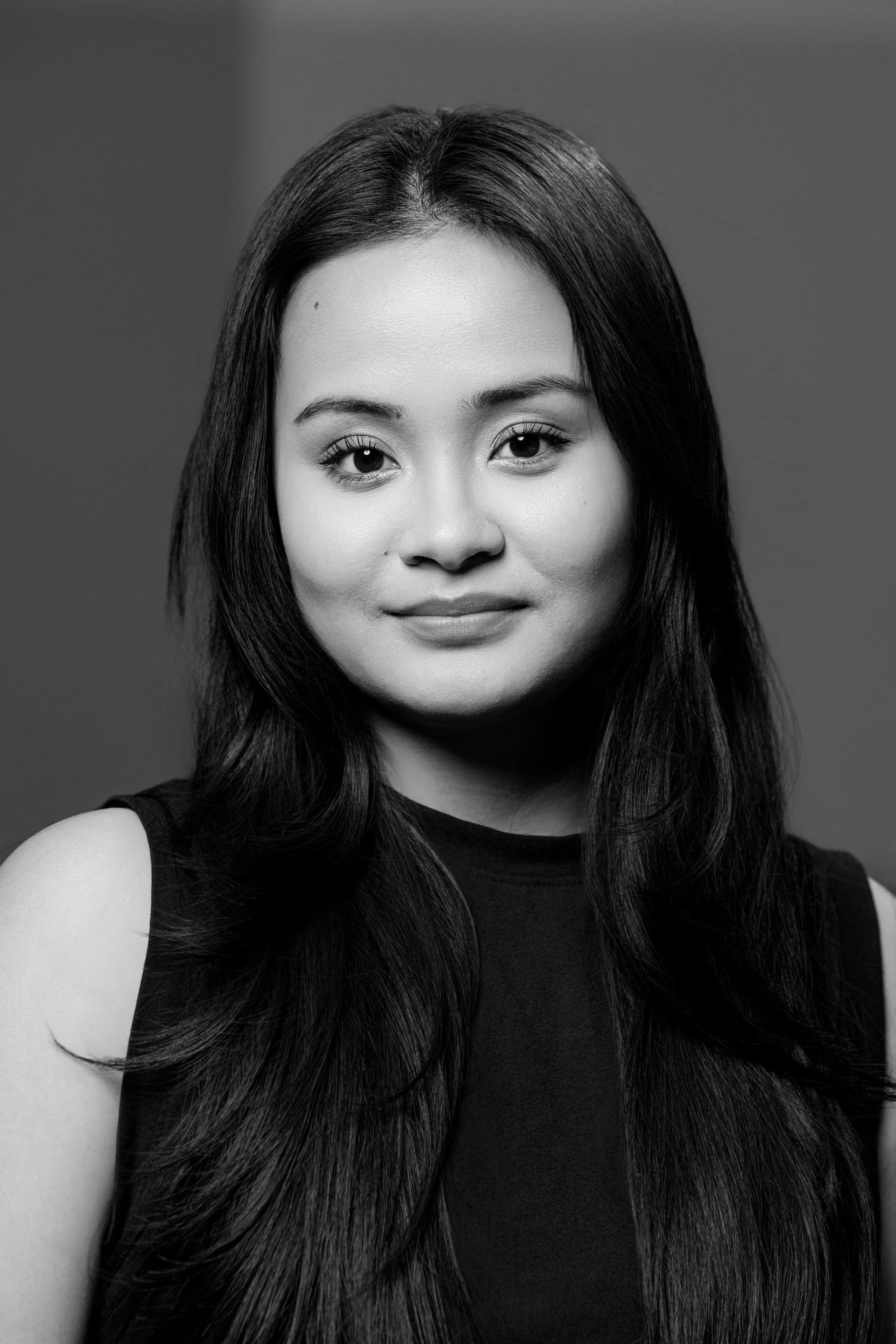 Black and white portrait of a woman with long dark hair, smiling slightly, wearing a sleeveless top.