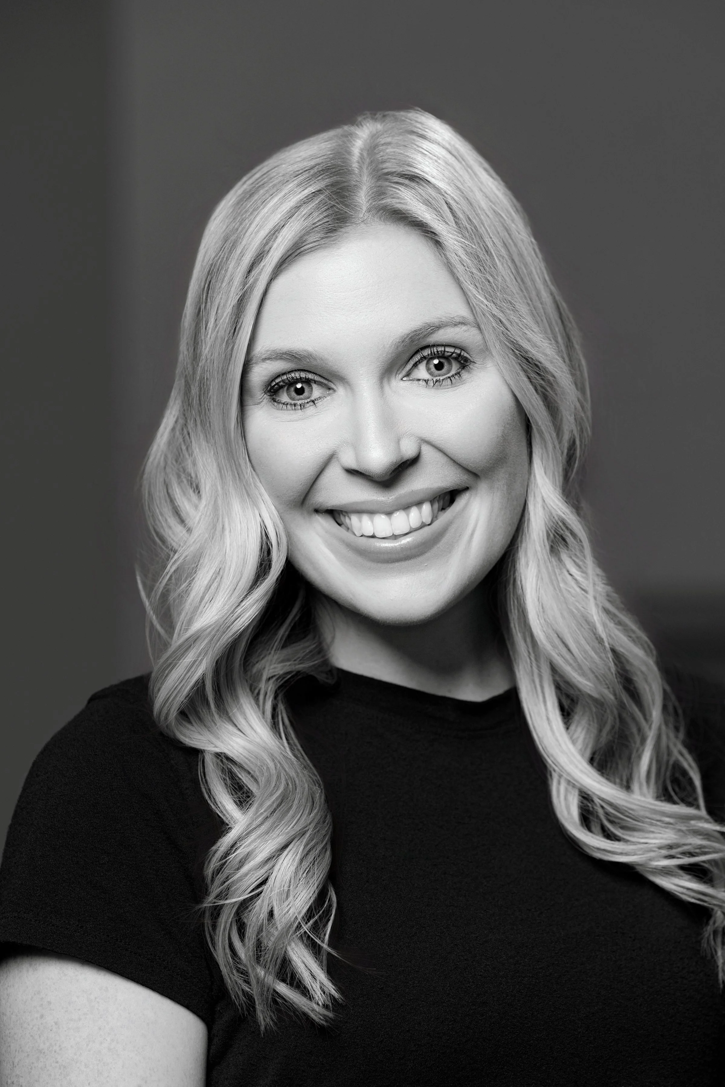 Black and white portrait of a smiling woman with long, wavy hair wearing a dark shirt.