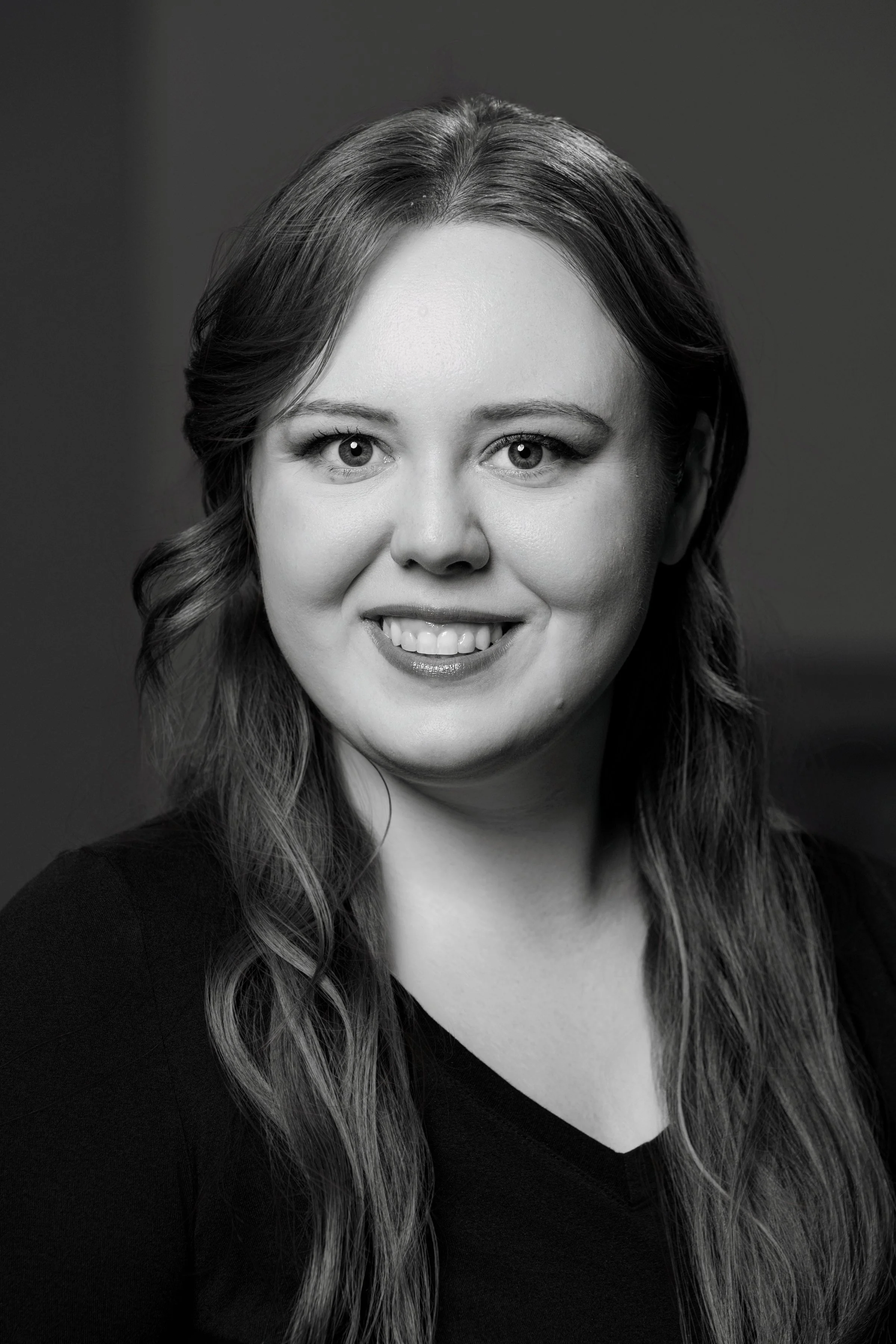 Black and white portrait of a smiling woman with long wavy hair, wearing a dark top.