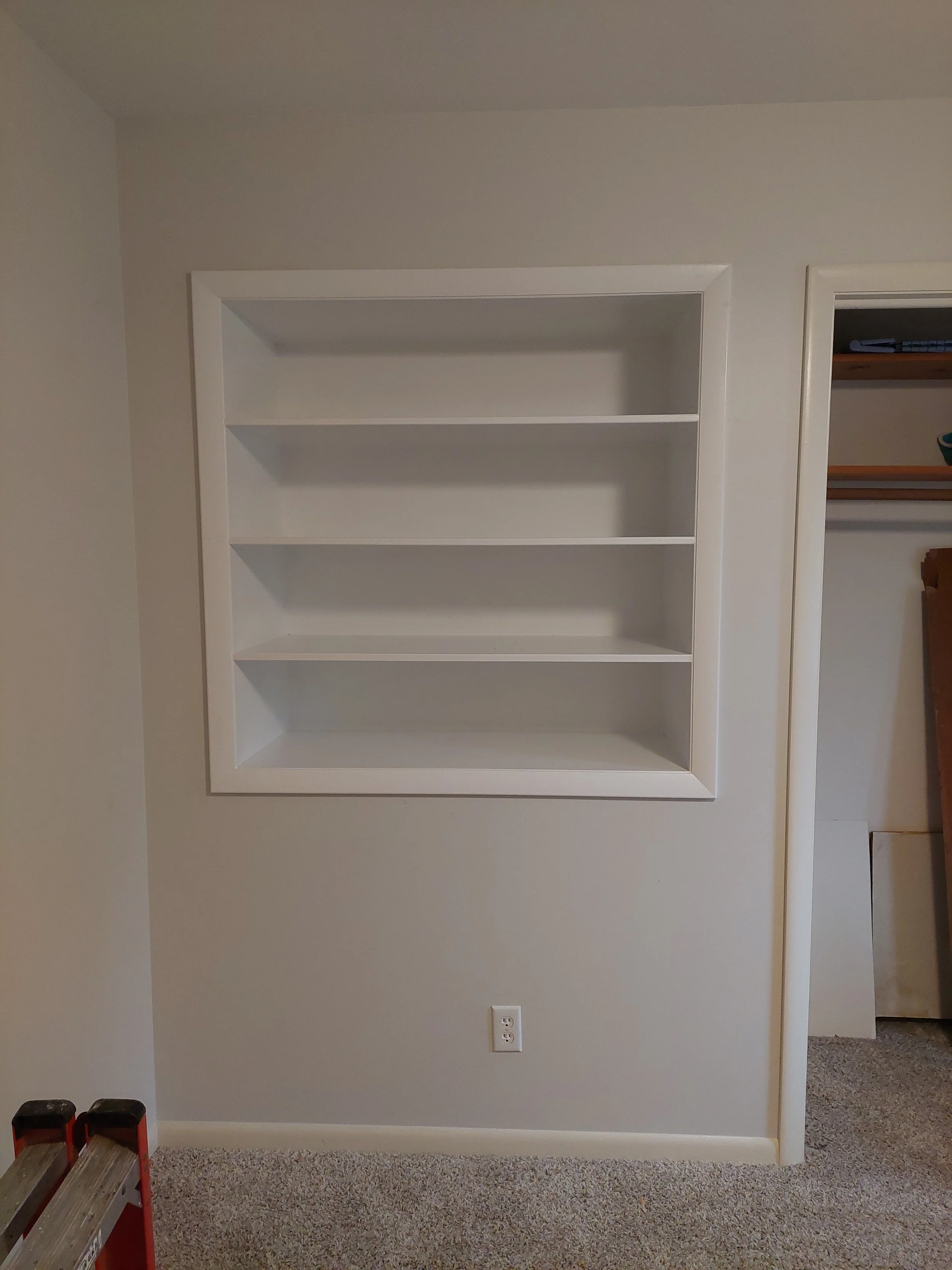 Custom built-in white wall-mounted bookshelf with four shelves, installed in wall