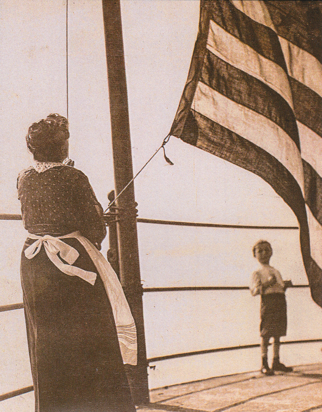 Jacob, Jr. watches as his grandmother, Kate Walker, hoists the flag at Robbins Reef, circa 1915. (Walker Family Collection)