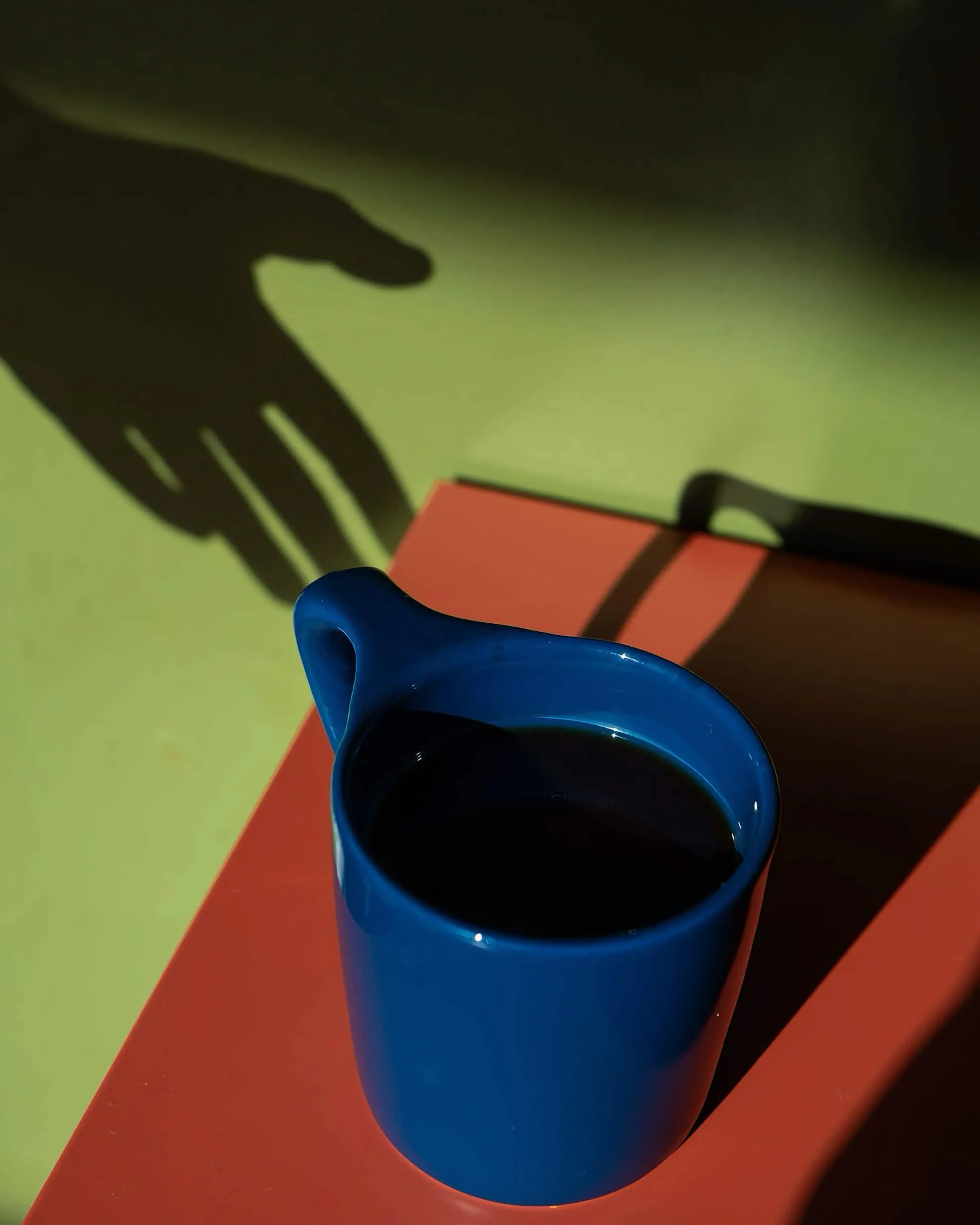 The shadow of a hand stretching toward a cup of coffee
