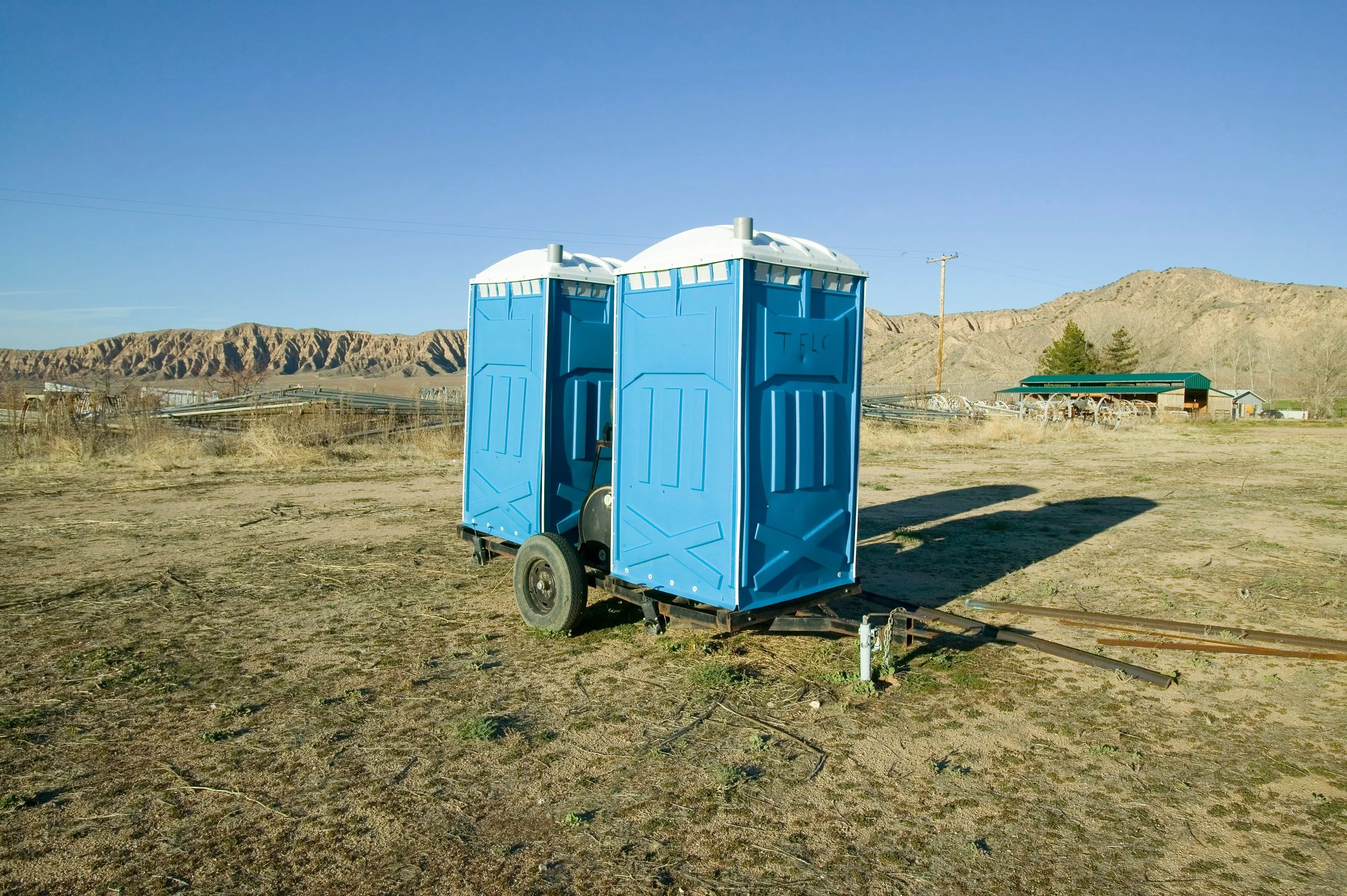 Two blue portable toilets on a trailer in an open field with mountains in the background.