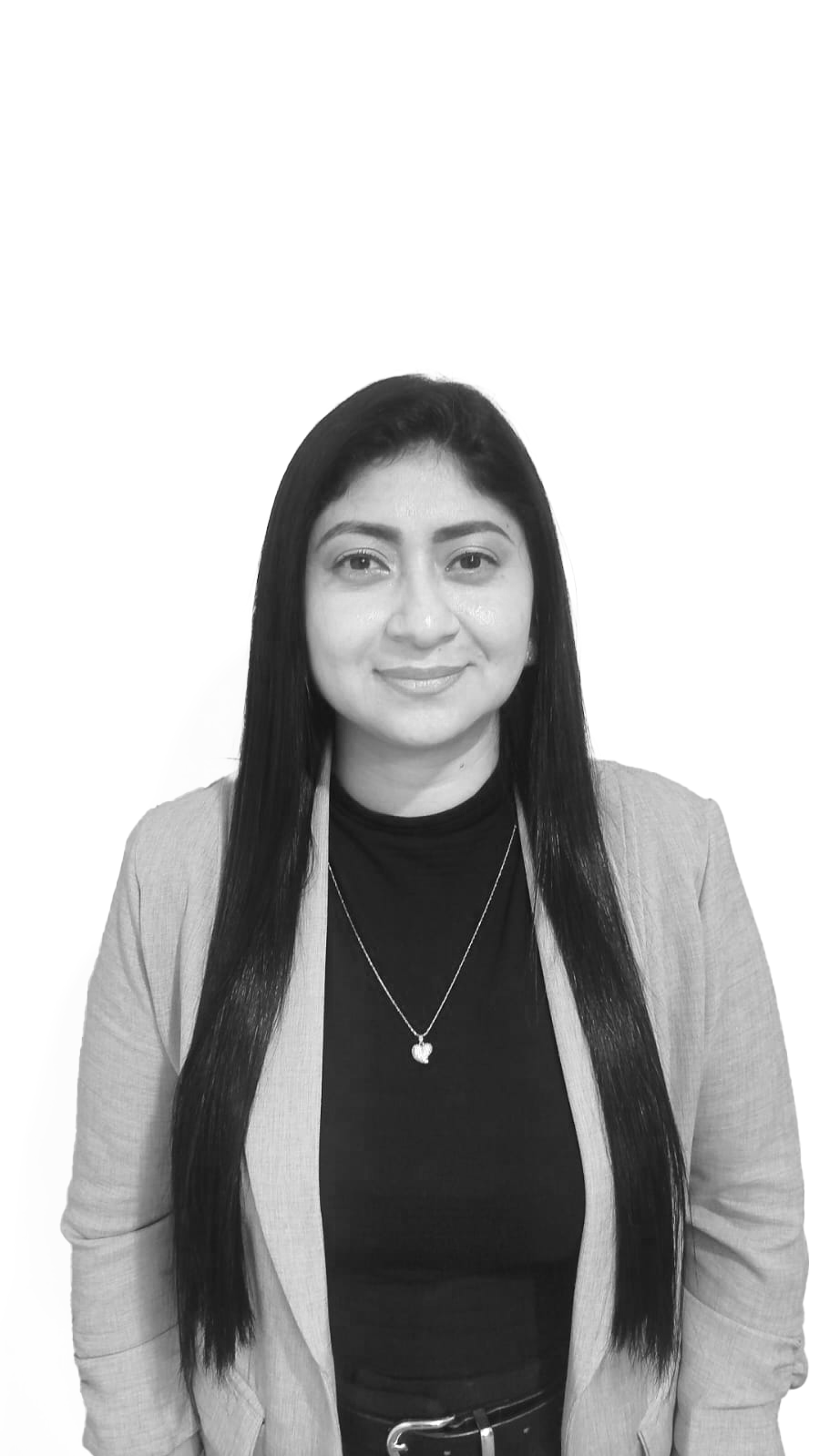 Black and white photo of a woman with long dark hair, smiling, wearing a blazer, a black top, and a necklace with an apple-shaped pendant, standing against a plain background.