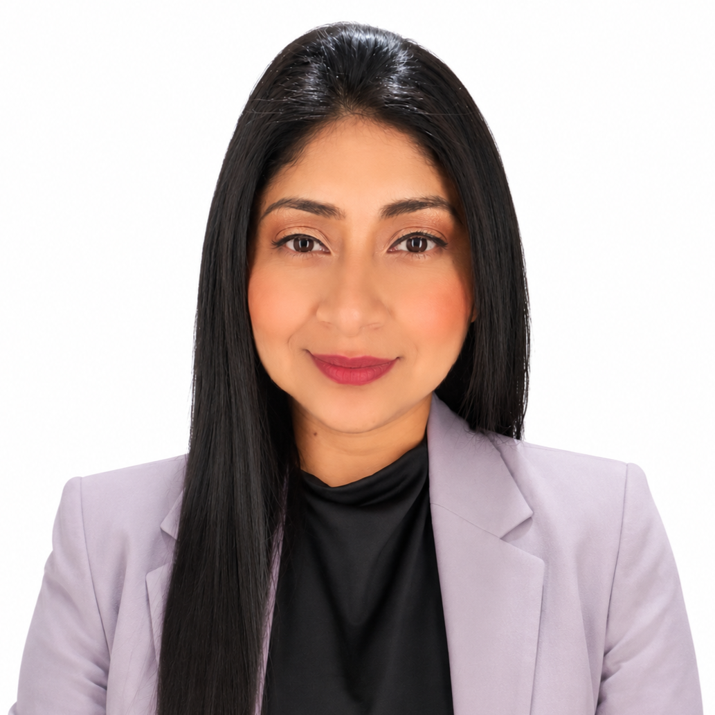 Black and white photo of a woman with long dark hair, smiling, wearing a blazer, a black top, and a necklace with an apple-shaped pendant, standing against a plain background.