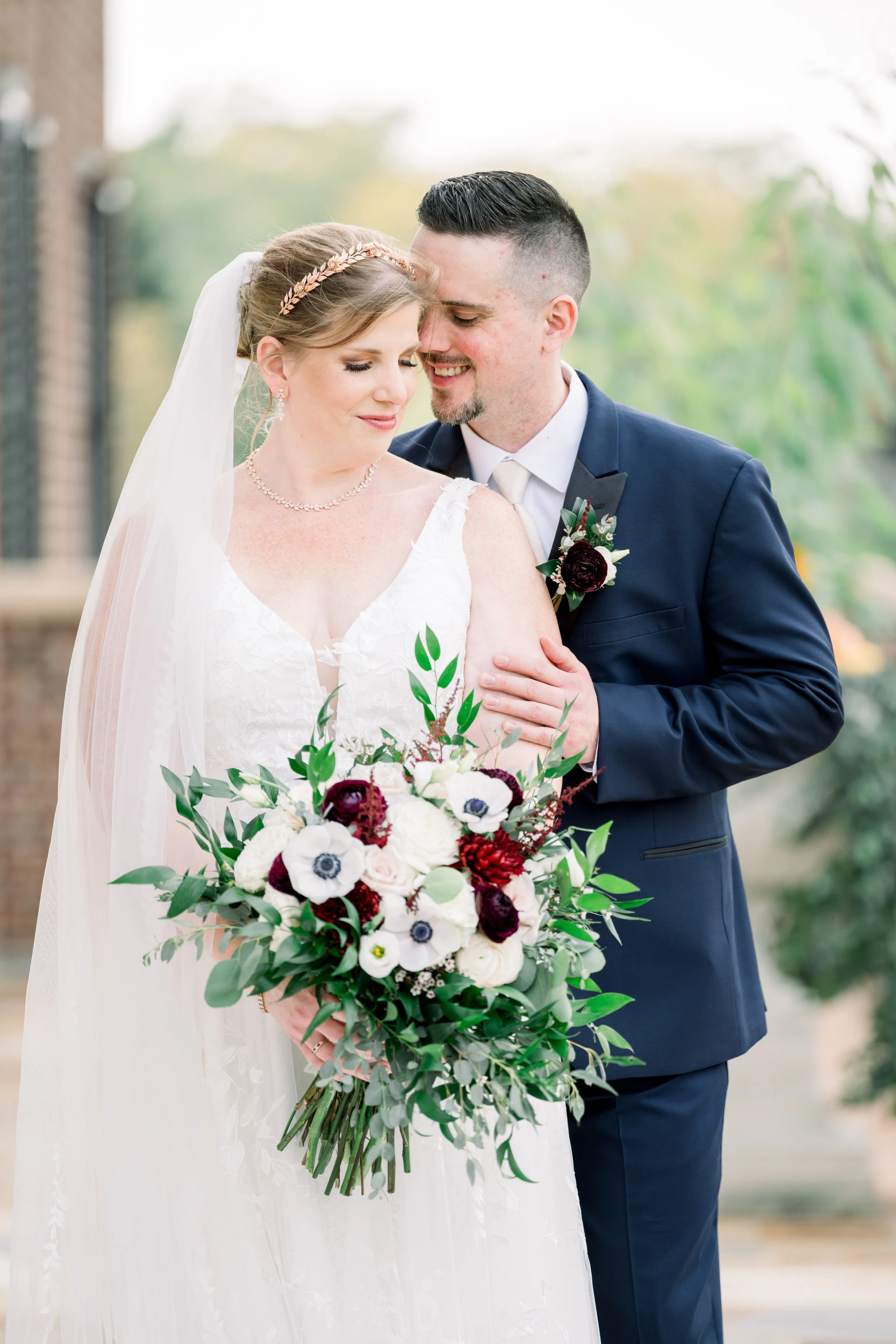 A fall bride holding a loose leaf bridal bouquet and a groom in a navy tuxedo posing at Cantigny in Wheaton, IL, during a stress-free autumn wedding day planned by One Fine Day Events.
