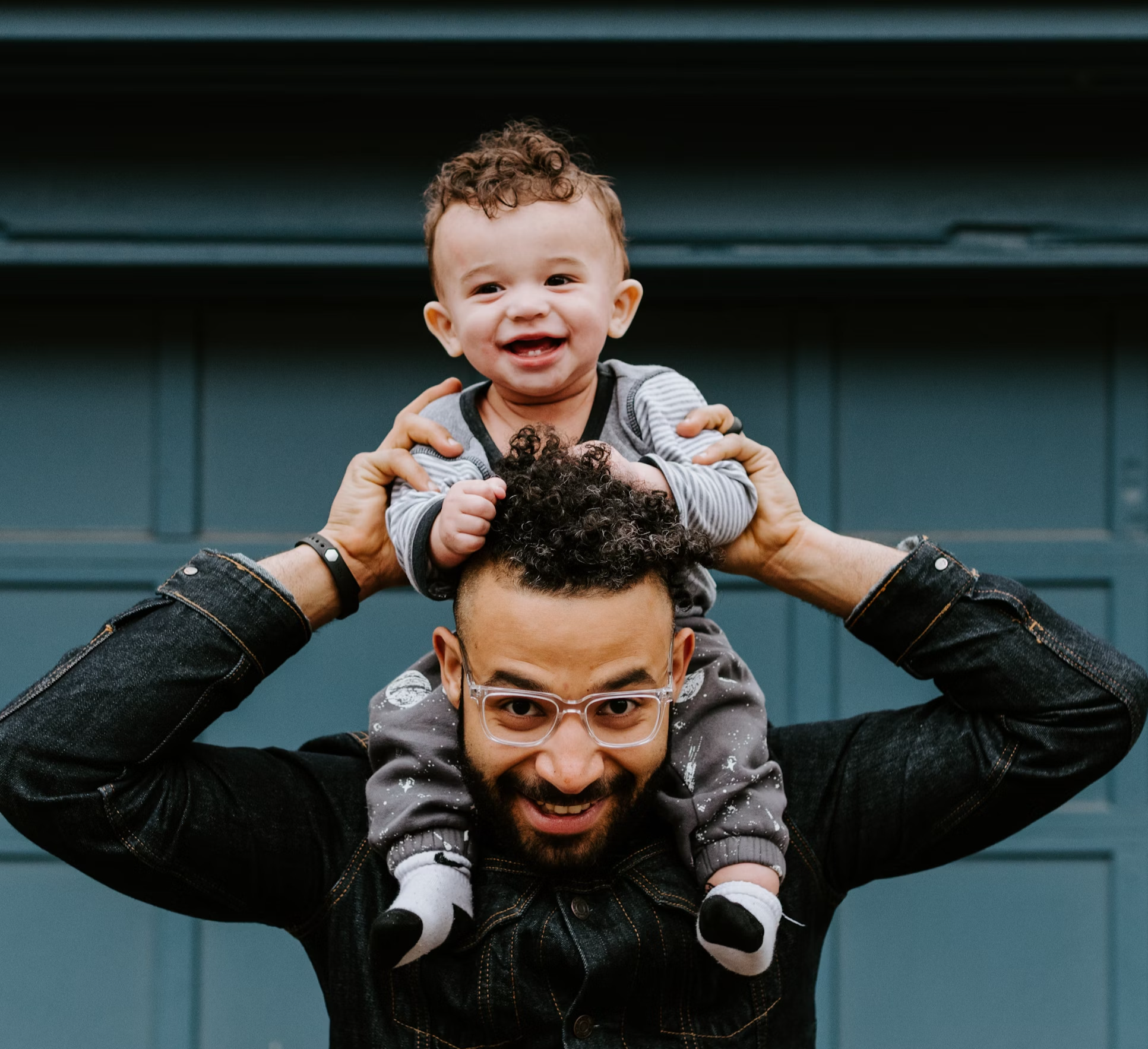 An ethnically diverse male holding a baby on his shoulders.