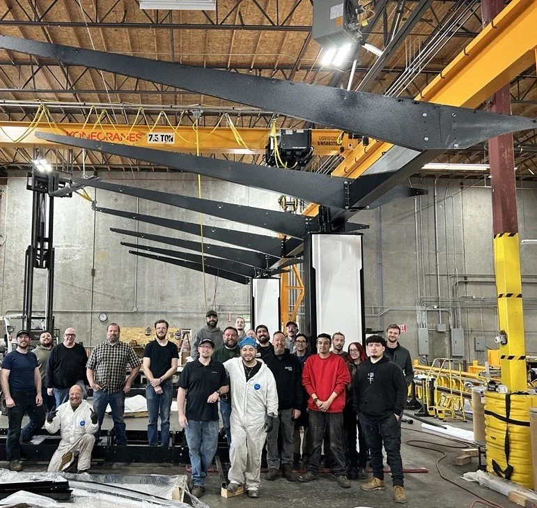Fulcrum team standing in front of a solar canopy structure under fabrication, showcasing large steel beams and support columns inside the manufacturing facility