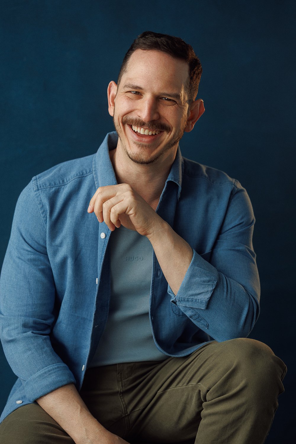 Man in blue shirt smiling against dark background